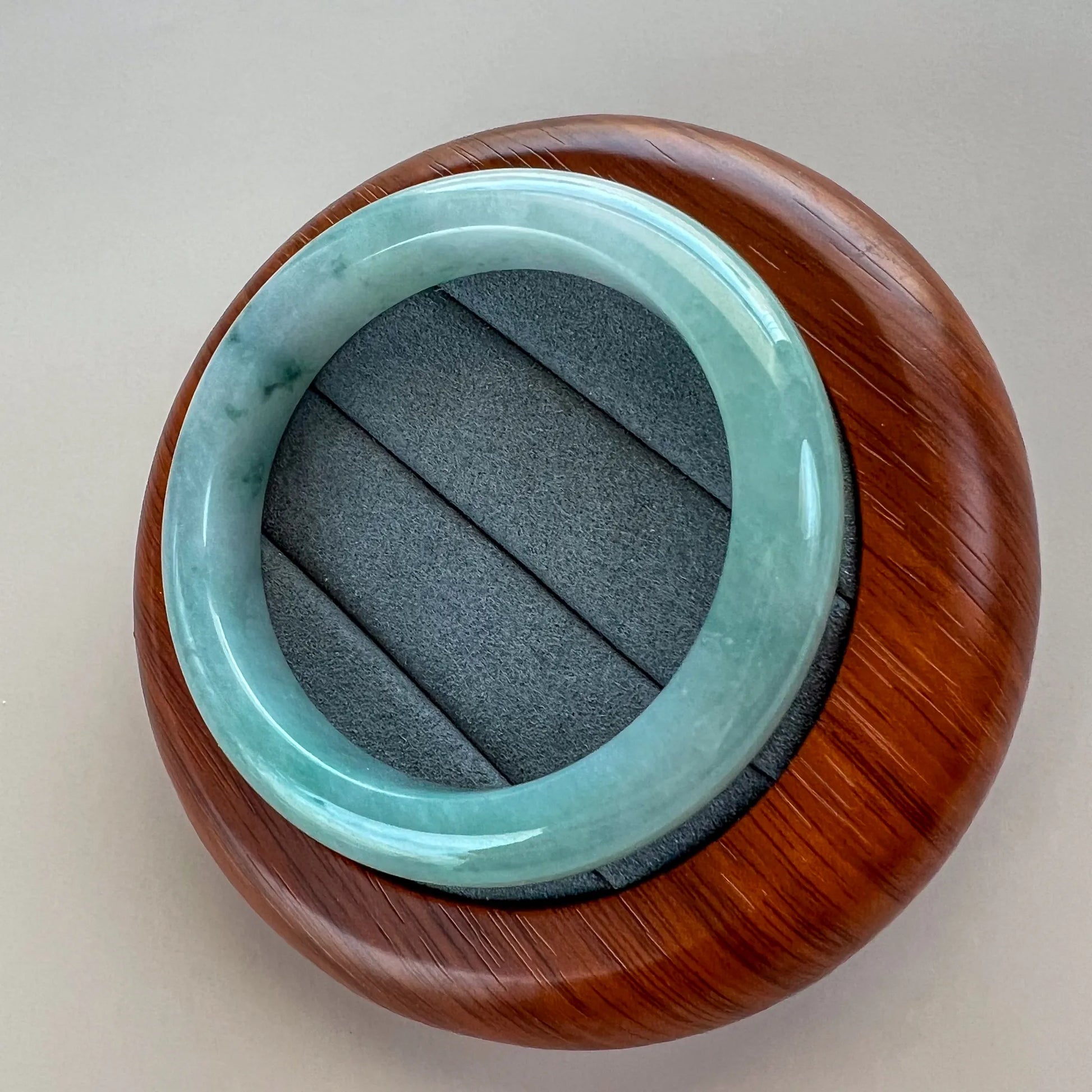 Angled view of polished jade bangle resting on a carved wood stand with gray cushion base.
