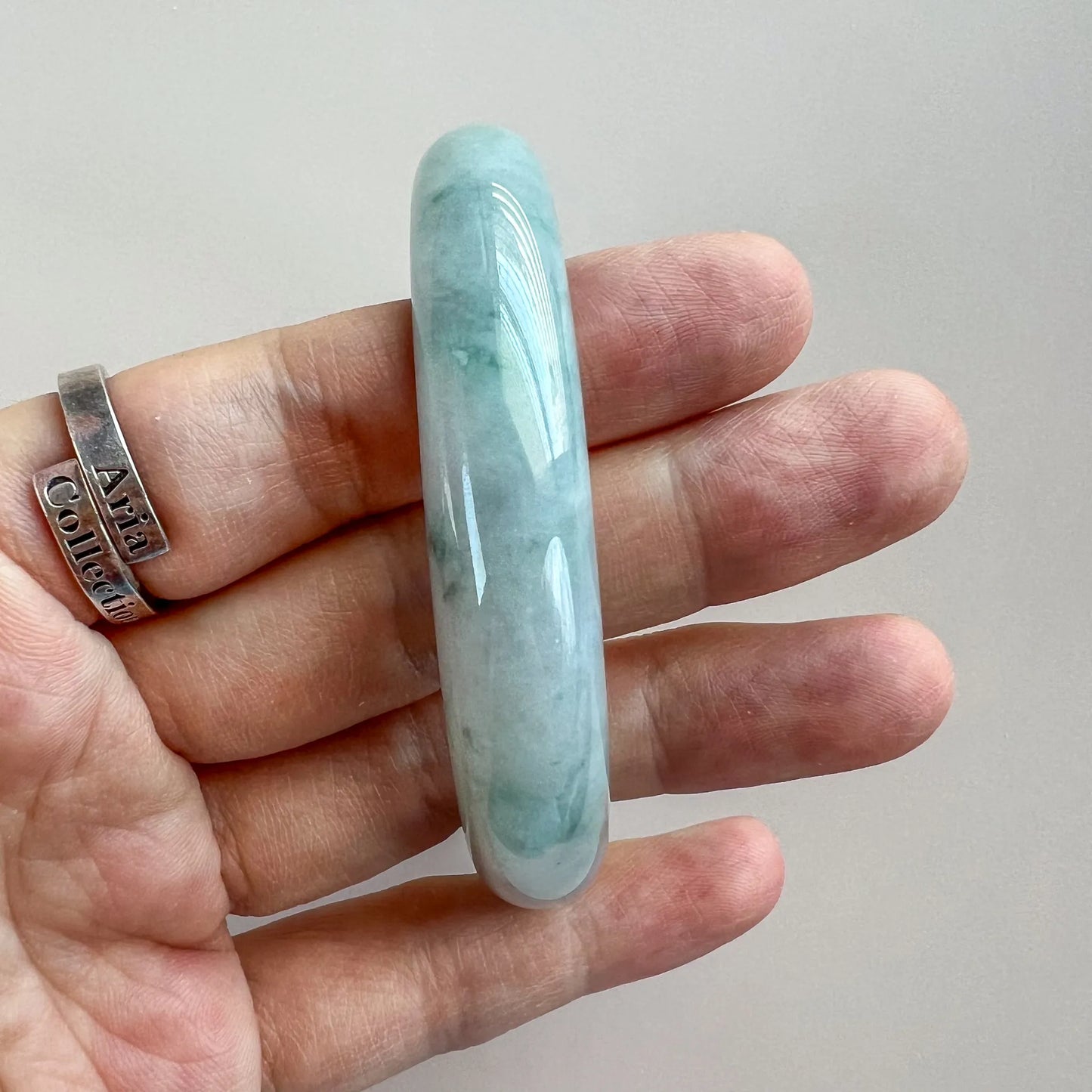 Side profile of smooth light green jade bangle, glossy finish, held in hand for scale.
