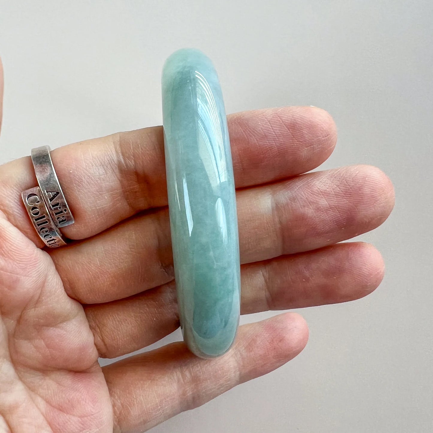 Side profile of polished pale green jade bangle, semi-translucent finish, shown in hand.
