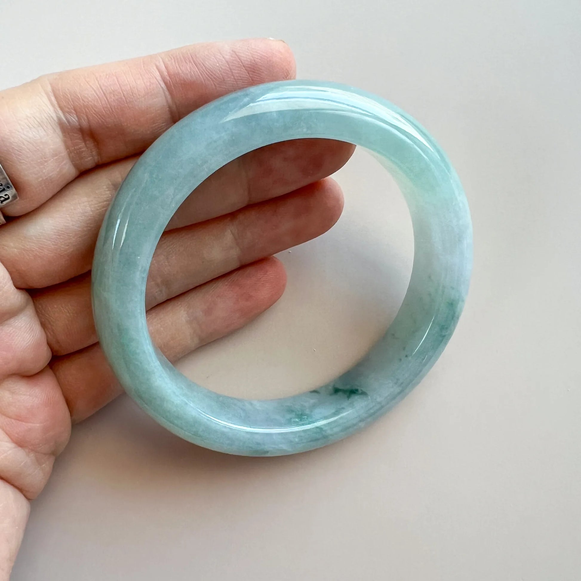 Handheld view of a light blue-green jade bangle, glossy round shape, minimal inclusions.