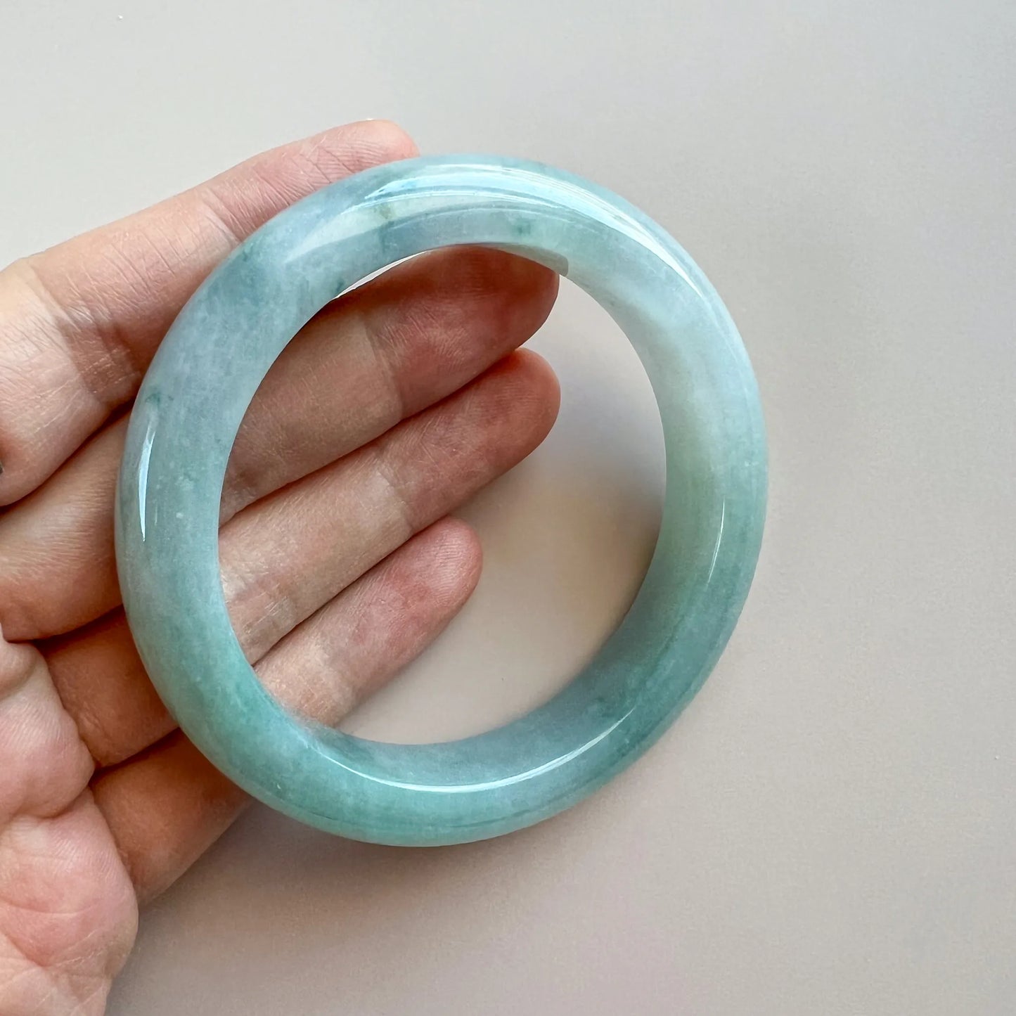 Angled handheld view of translucent aqua jade bangle with smooth polished finish.