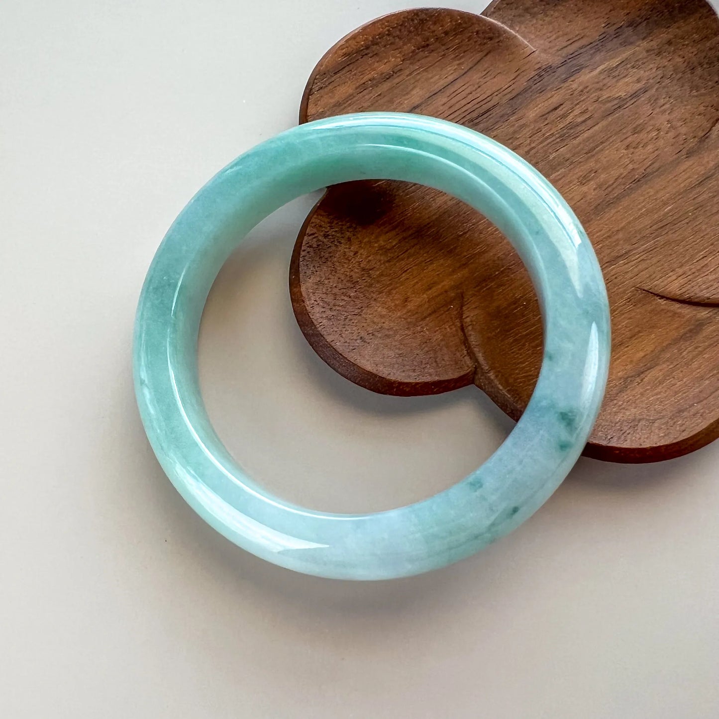 Front view of pale green jade bangle on a wood display surface, polished and rounded.