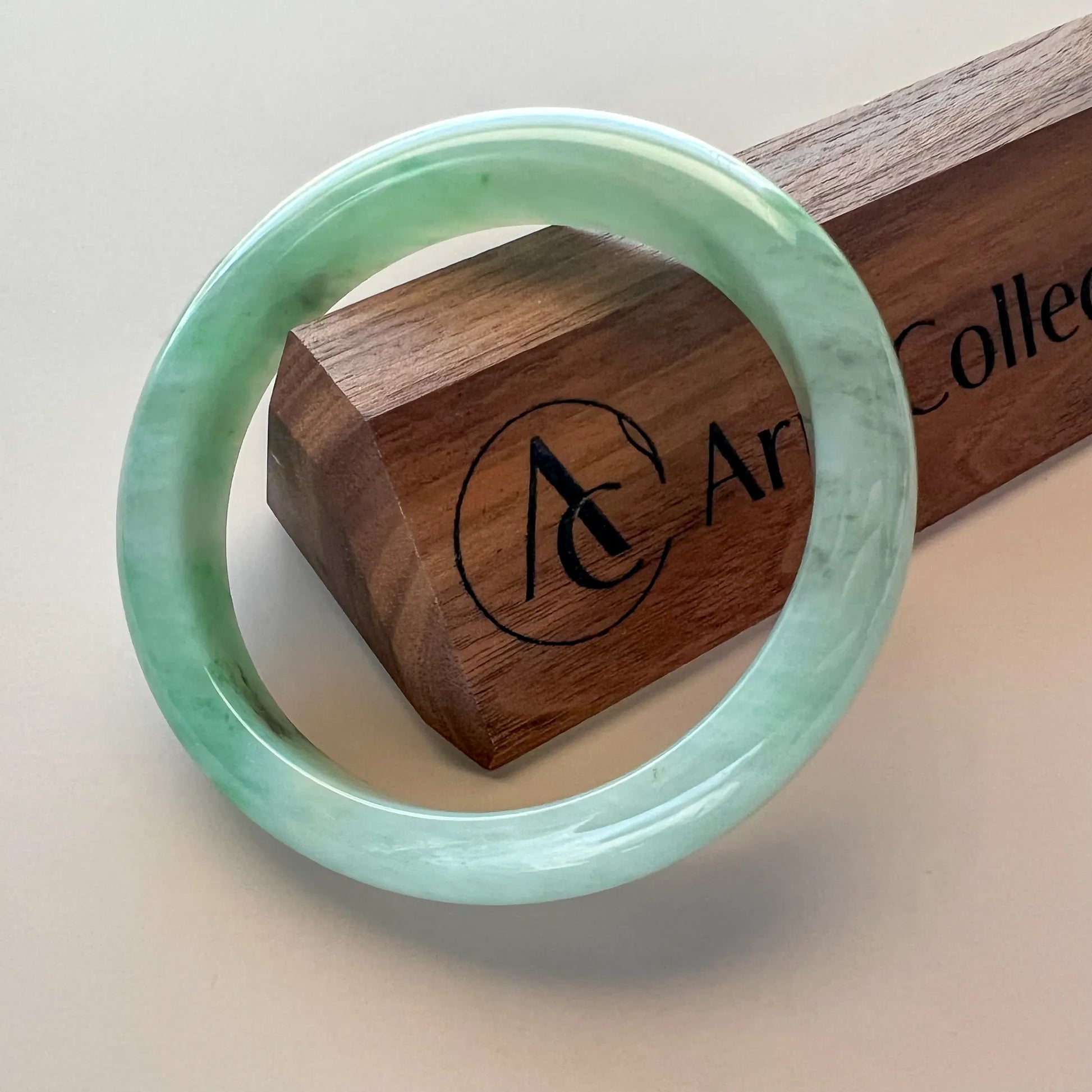 Polished green jade bangle front view with natural mottling on a wooden box
