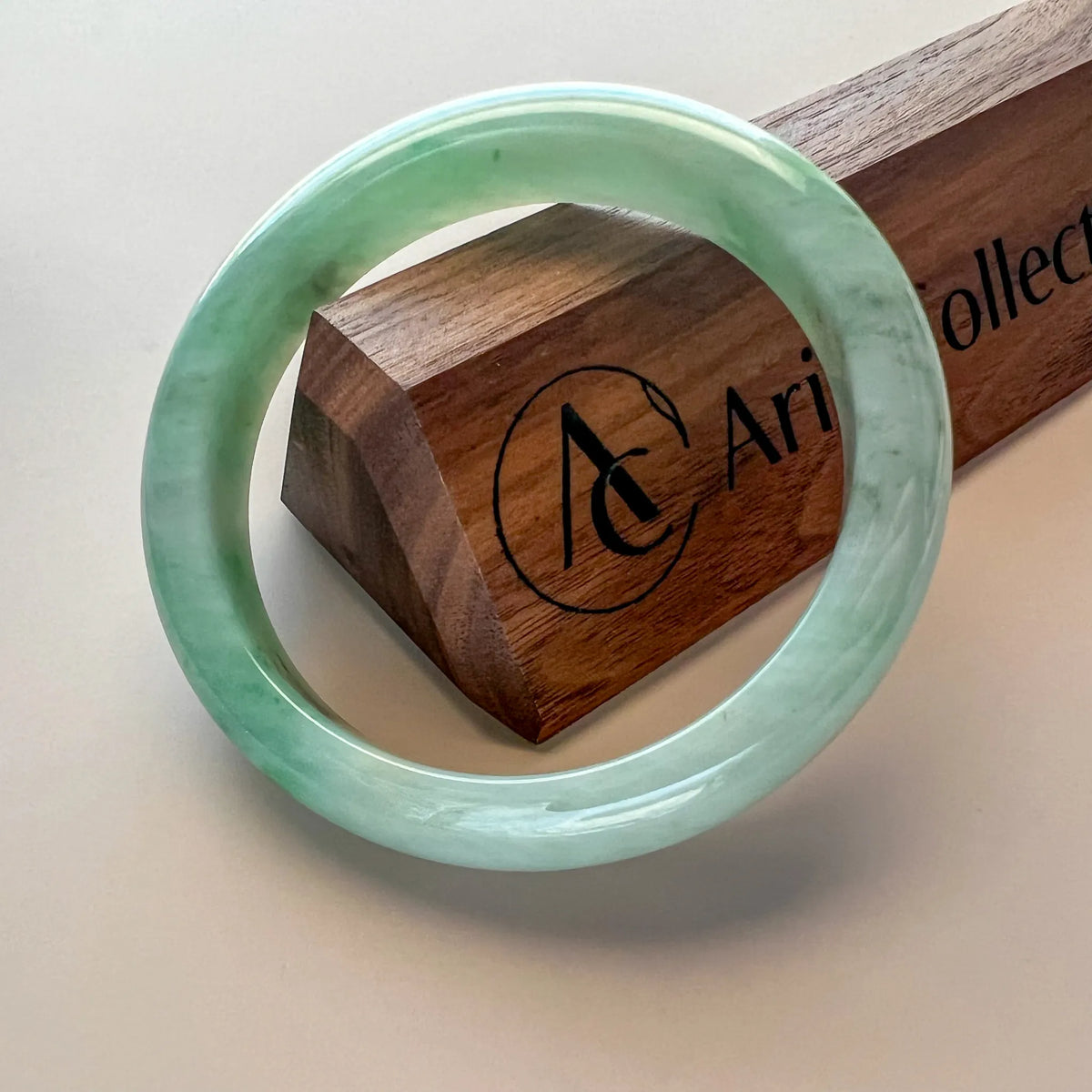 Smooth green jade bangle angled on branded wooden presentation box