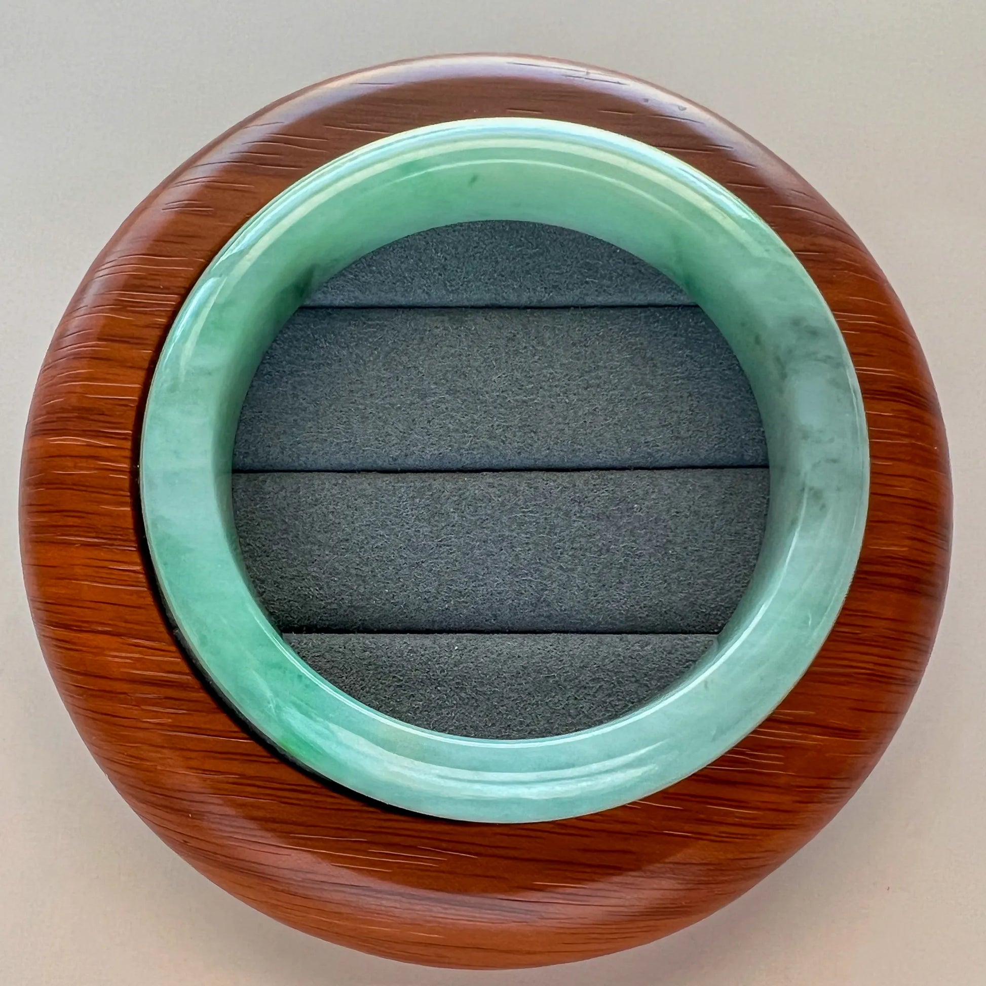 Round green jade bangle displayed on a wood stand with gray padded insert