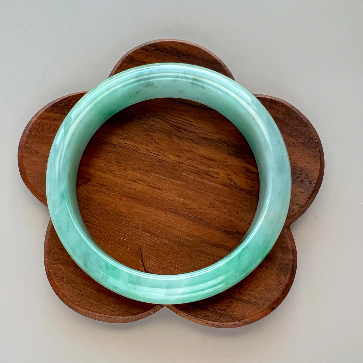 Polished green jade bangle resting on a flower-shaped wooden base