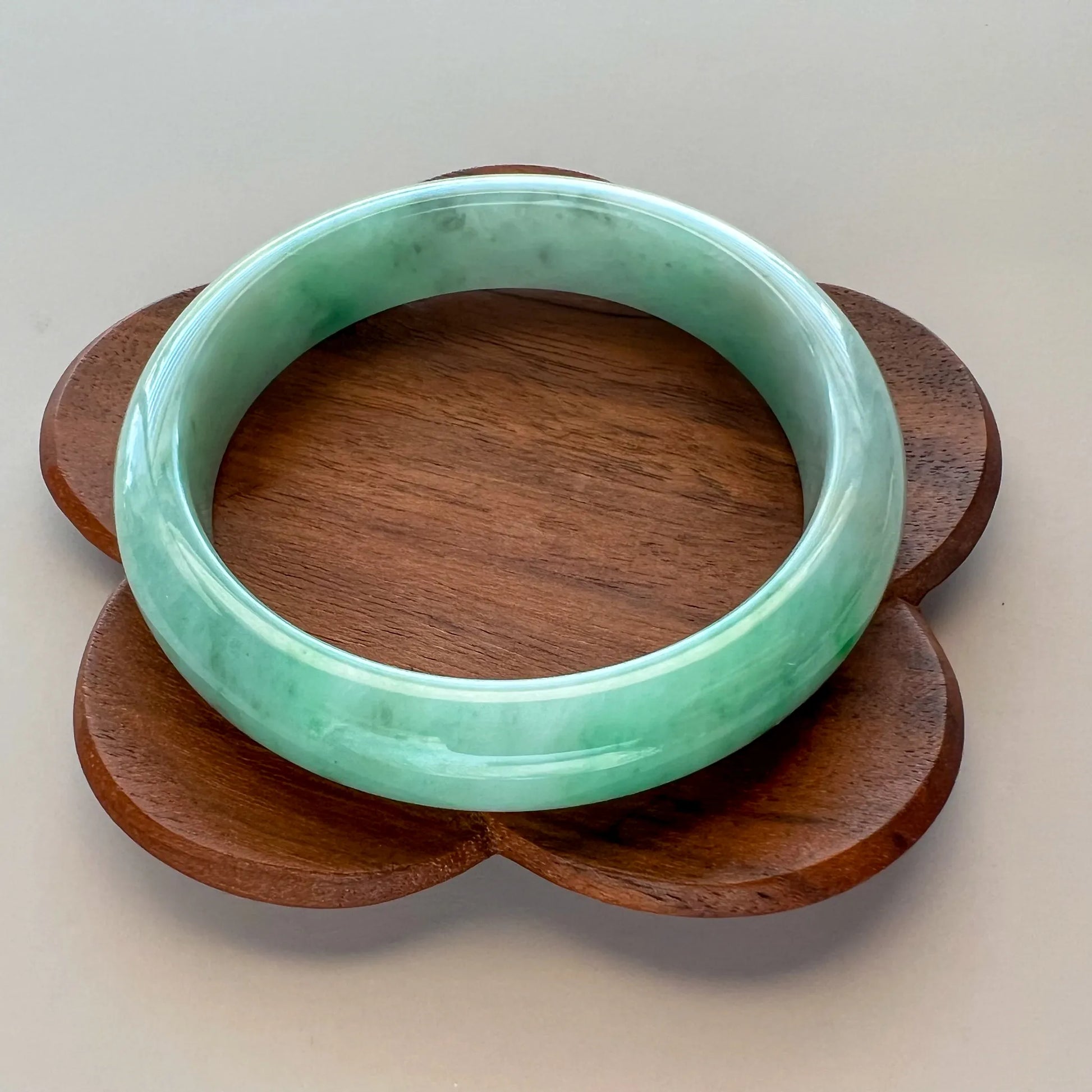 Glossy pale green jade bangle on carved wooden display stand
