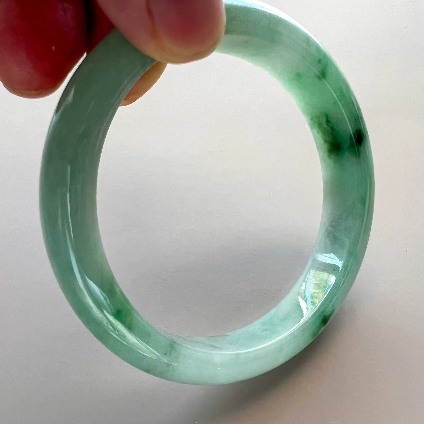 Side view of translucent light green jadeite bangle showing darker green accents and a glossy surface