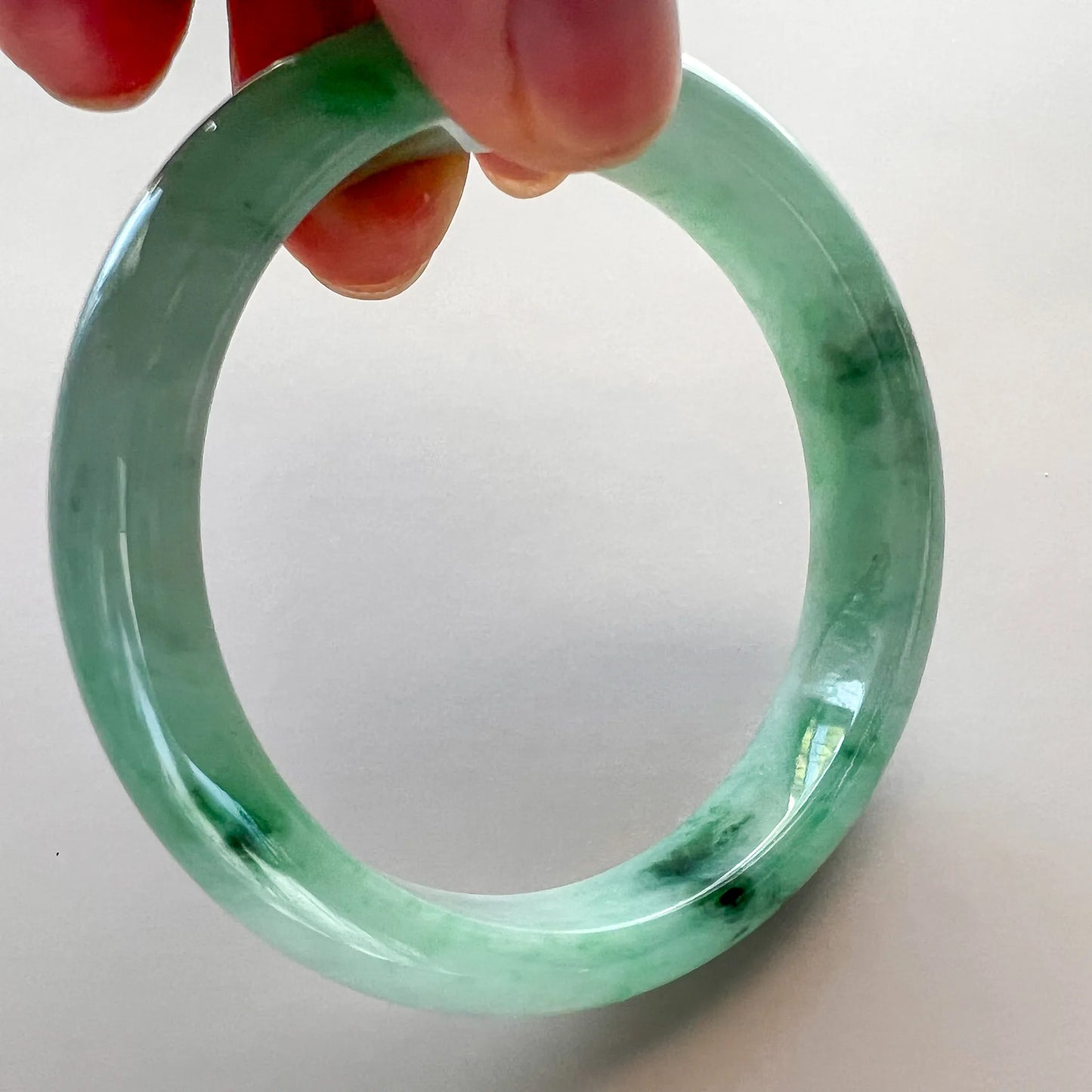 Close-up of translucent green jade bangle showing dark inclusions