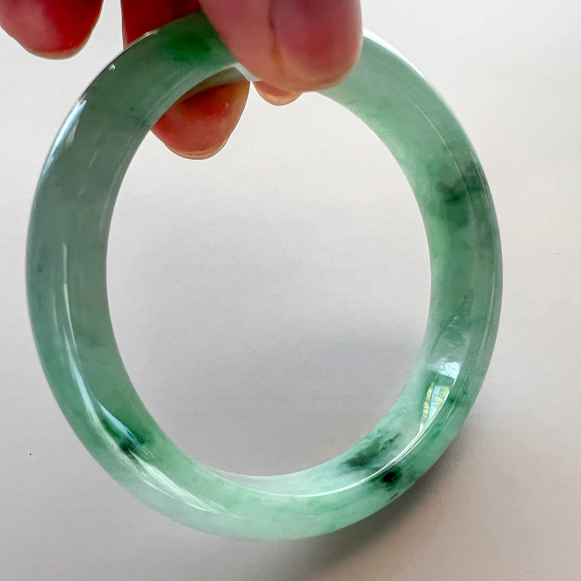 Close-up of translucent green jade bangle showing dark inclusions