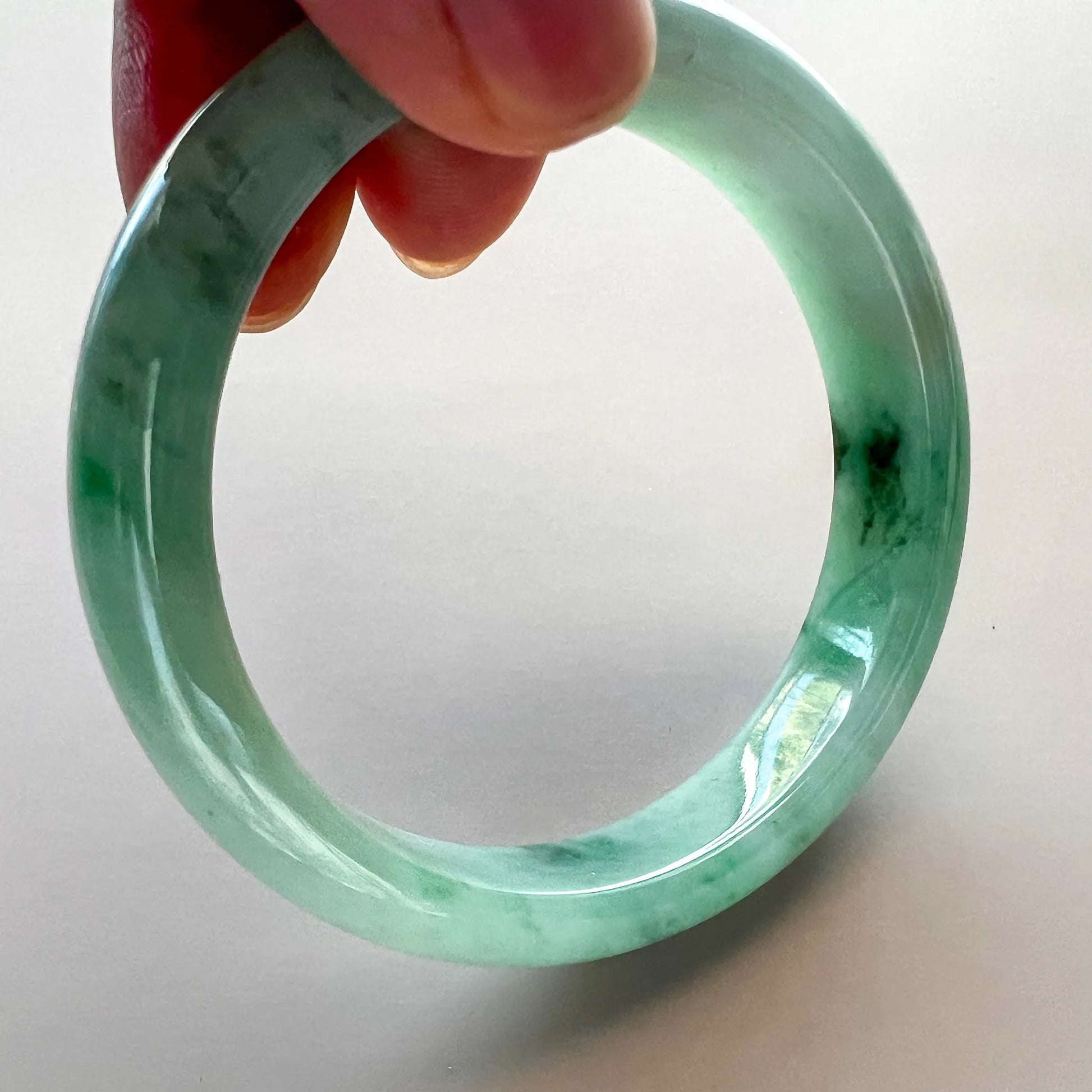 Handheld close-up of polished green jade bangle with natural inclusions