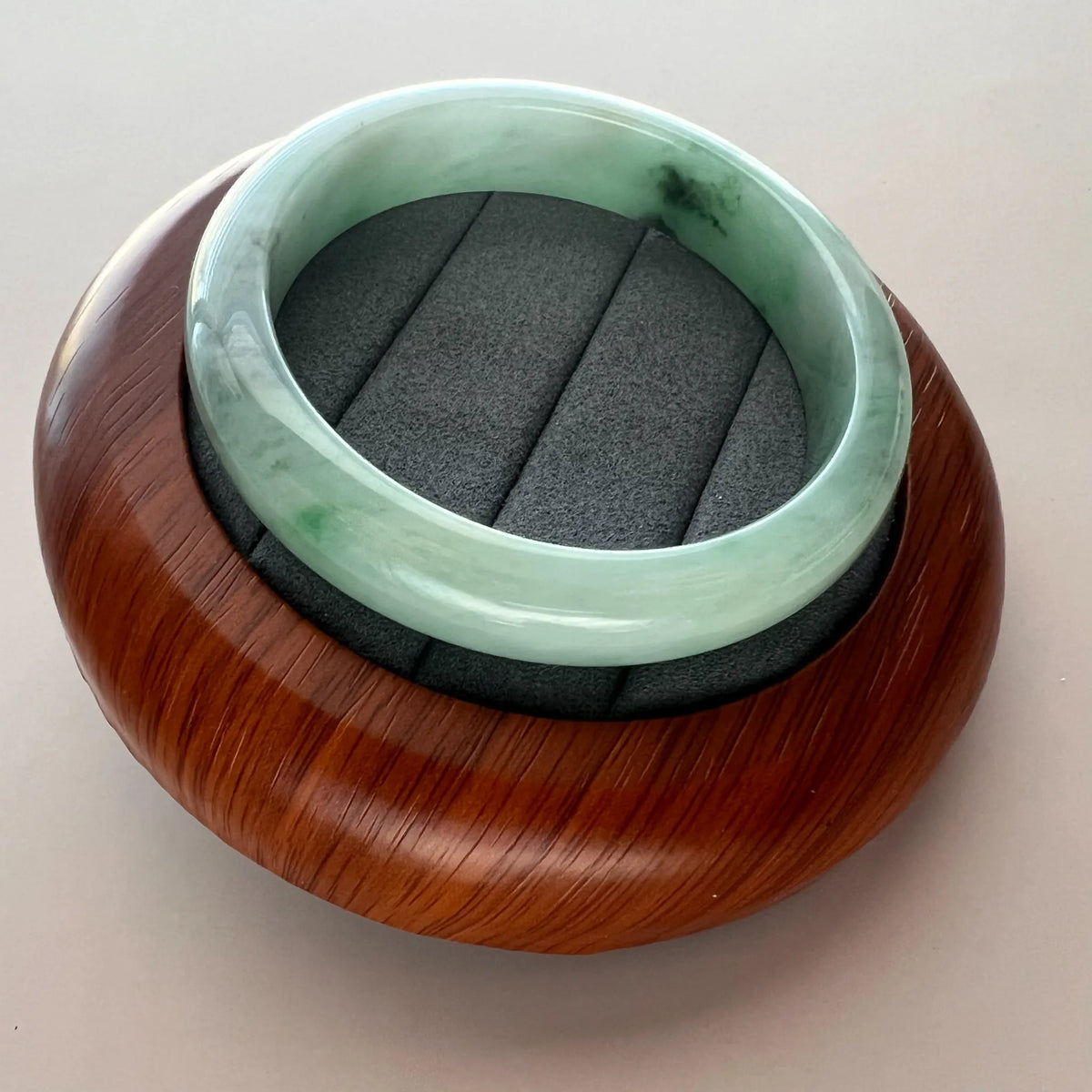 Light green Burmese Type A jadeite bangle shown at an angle on a wooden display stand with smooth polished finish