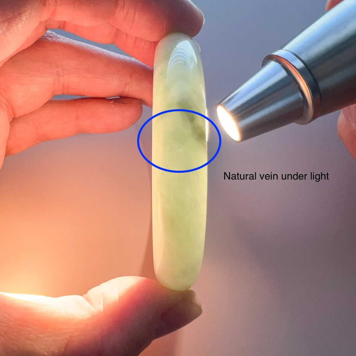 Light green jadeite bangle held under flashlight, showing translucent polished finish and natural vein detail