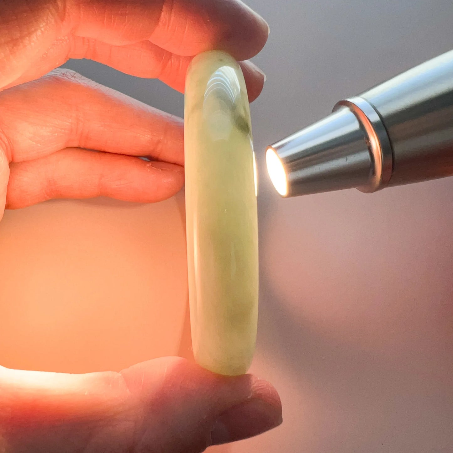 Close-up side view of light green jadeite bangle held by hand, polished translucent finish under flashlight