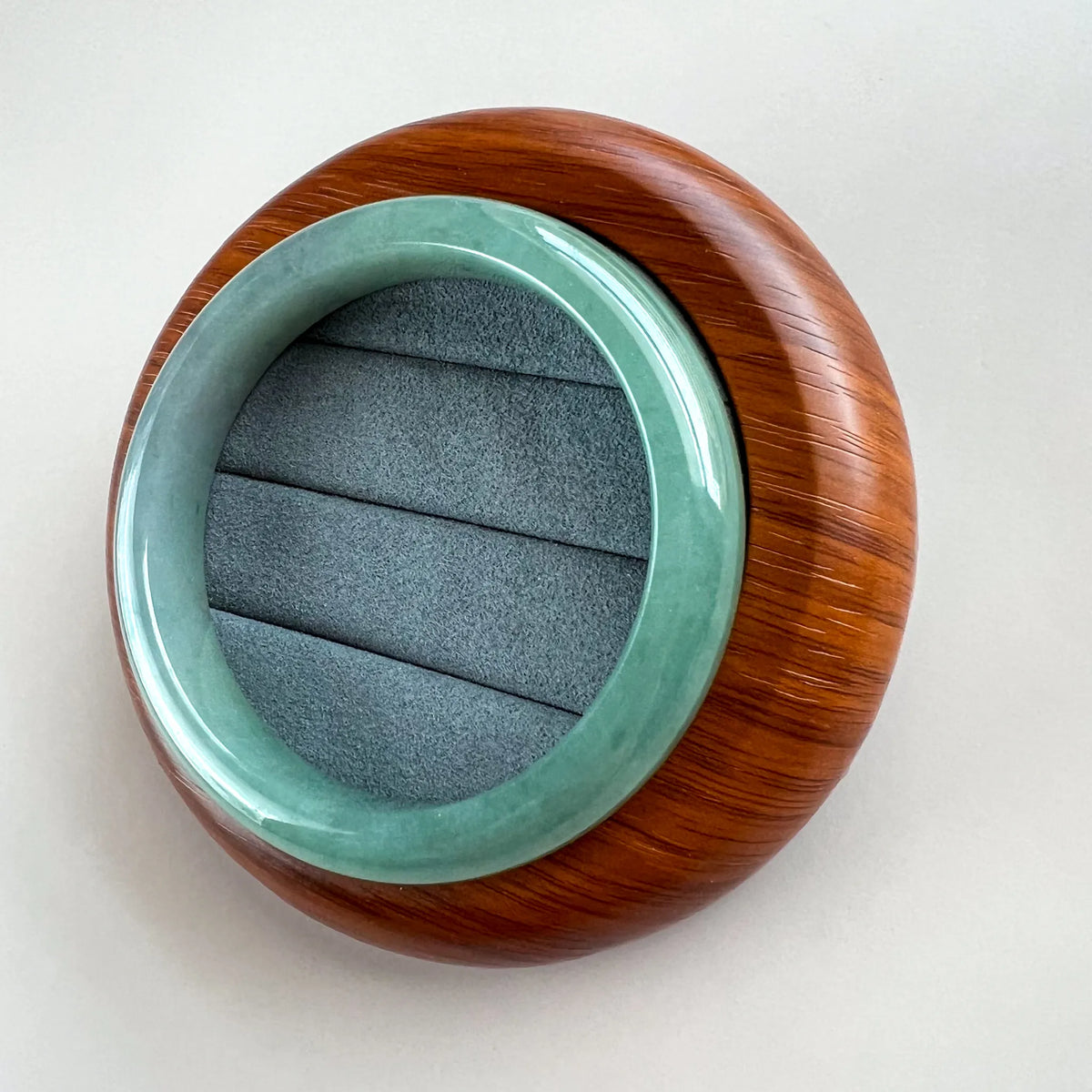 Angled view of smooth jade bangle on a carved wood display stand