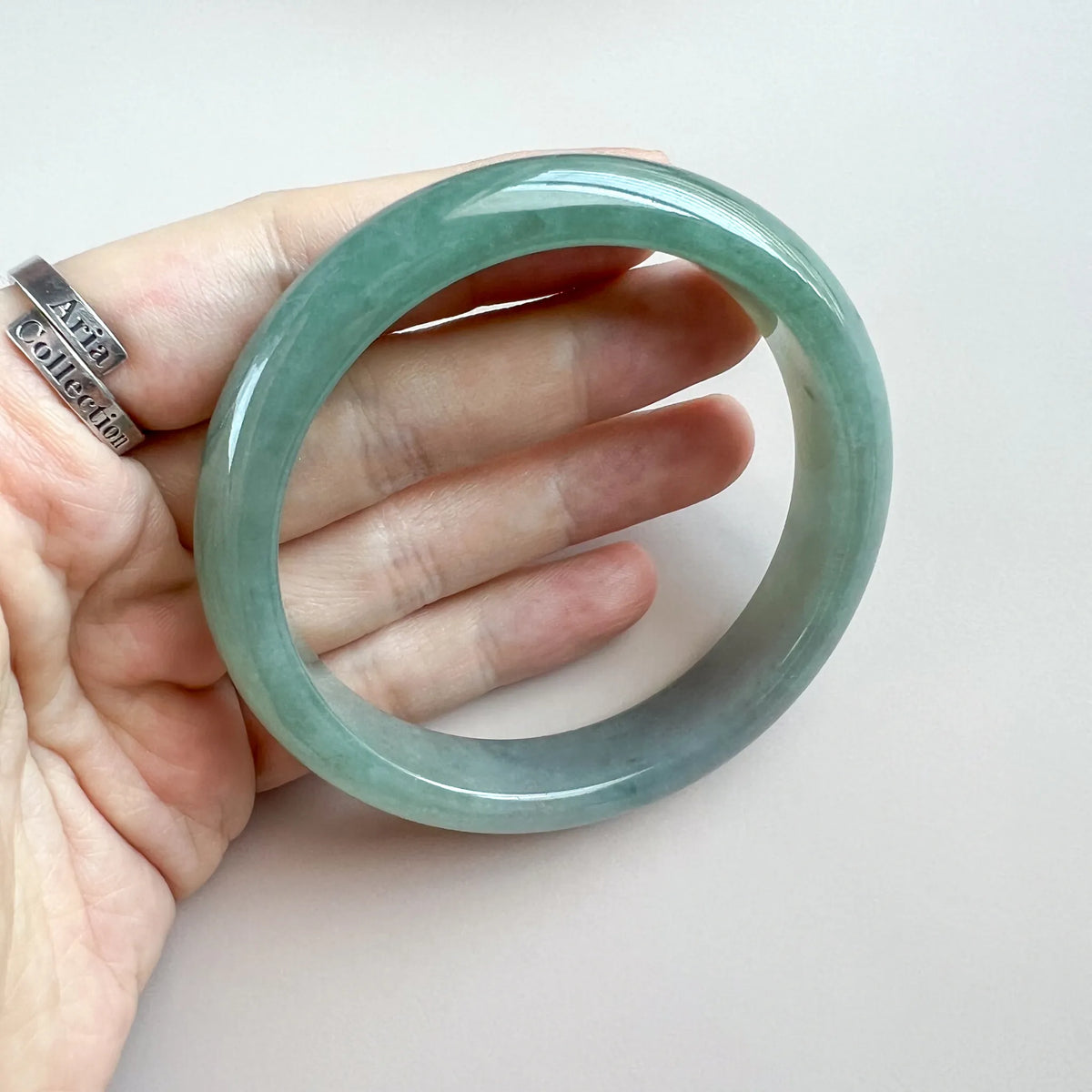 Hand-held view of polished green jade bangle showing round profile and glossy finish