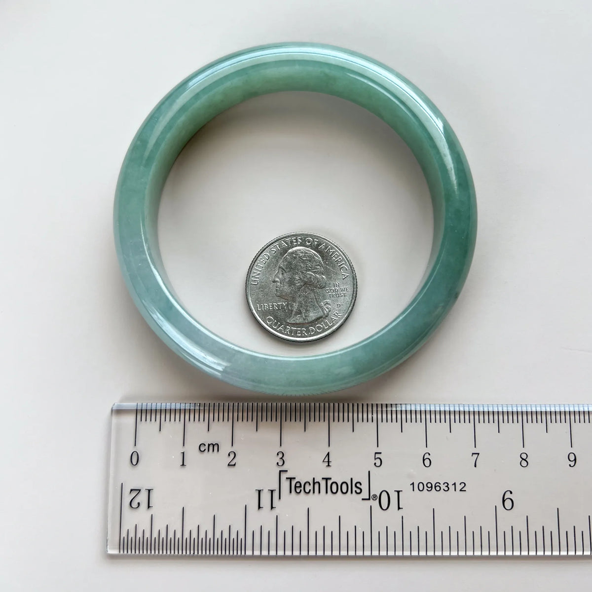 Top view of the translucent green-blue jadeite bangle beside a ruler and quarter for scale