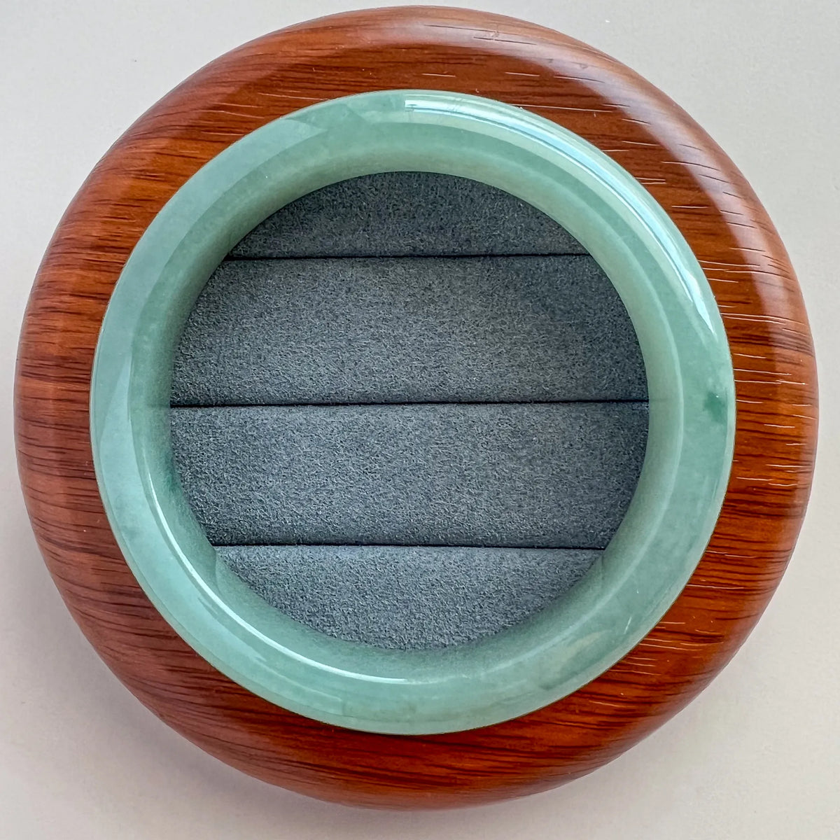 Top view of polished jade bangle displayed on a wooden stand with gray velvet insert