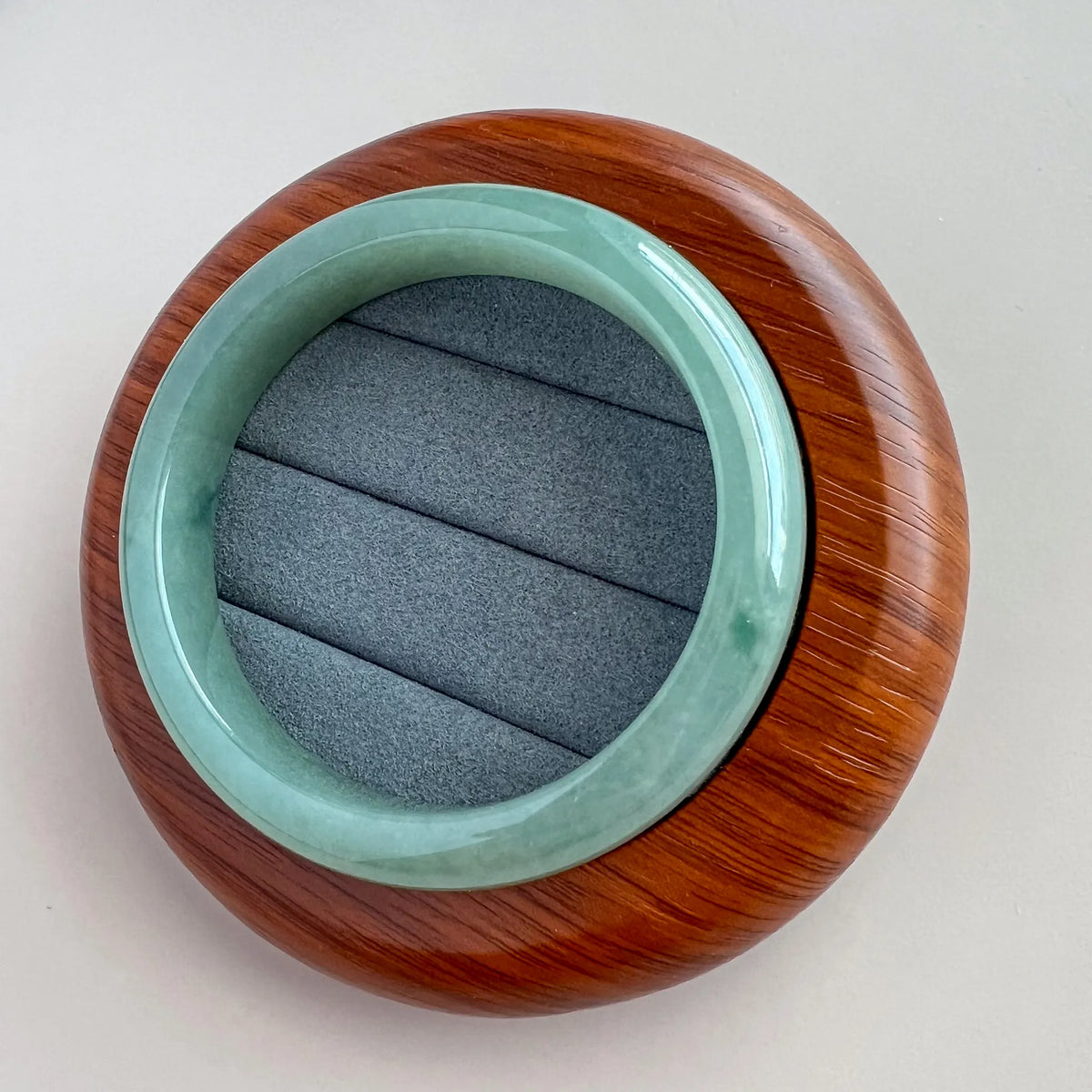 Angled view of glossy green jade bangle resting on a rounded wooden display base