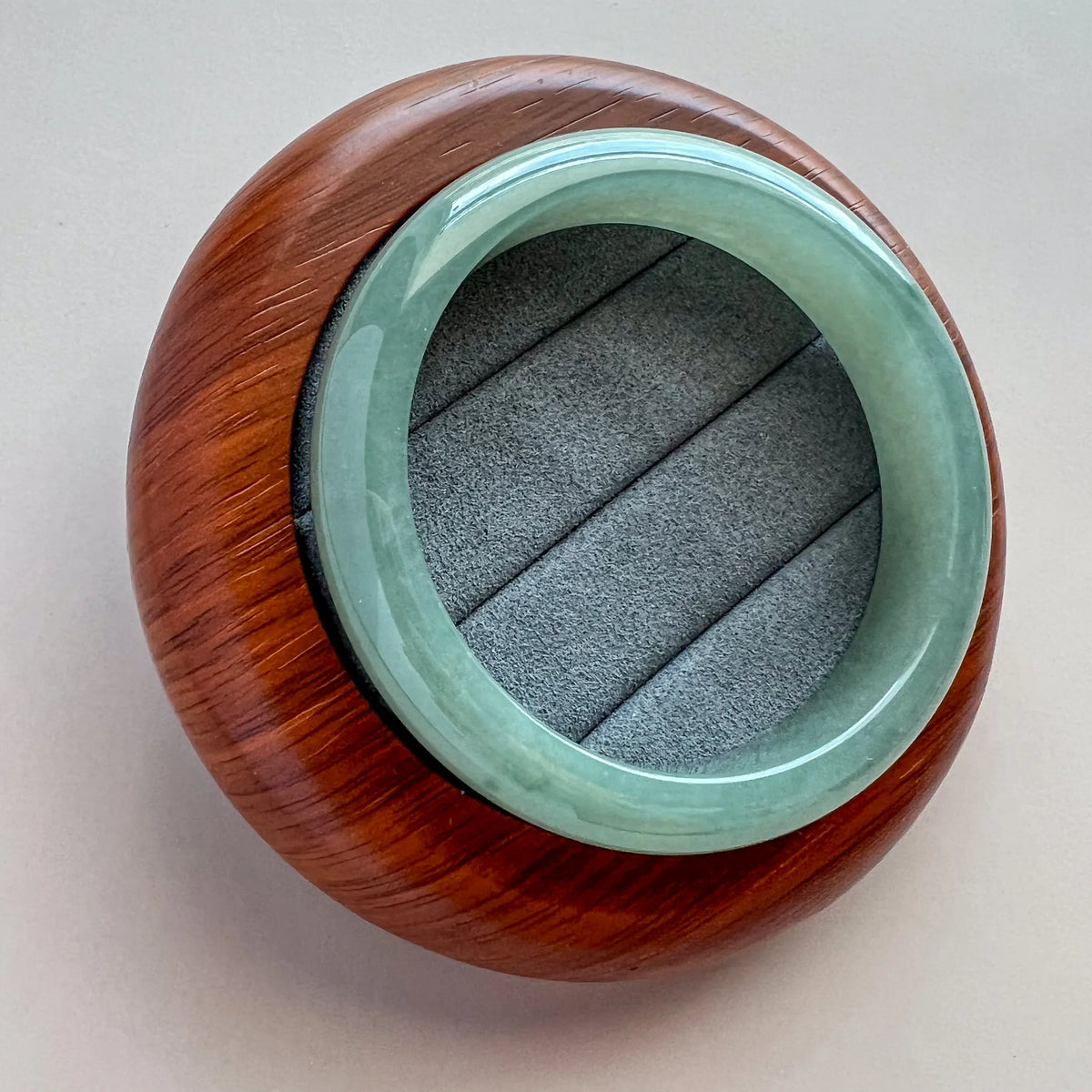 Polished green jade bangle shown on a wooden stand with smooth rounded profile