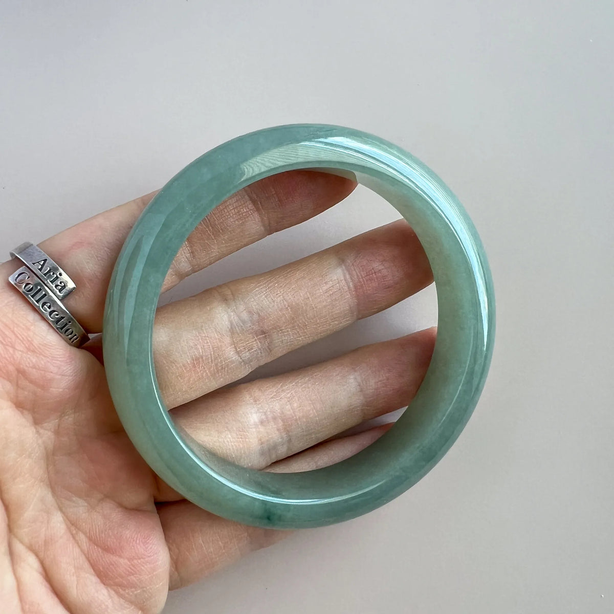 Jade bangle held in hand showing translucent green stone and high-gloss polished finish