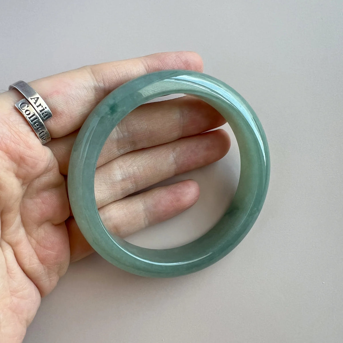 Close hand-held view of translucent green jade bangle with smooth rounded edges
