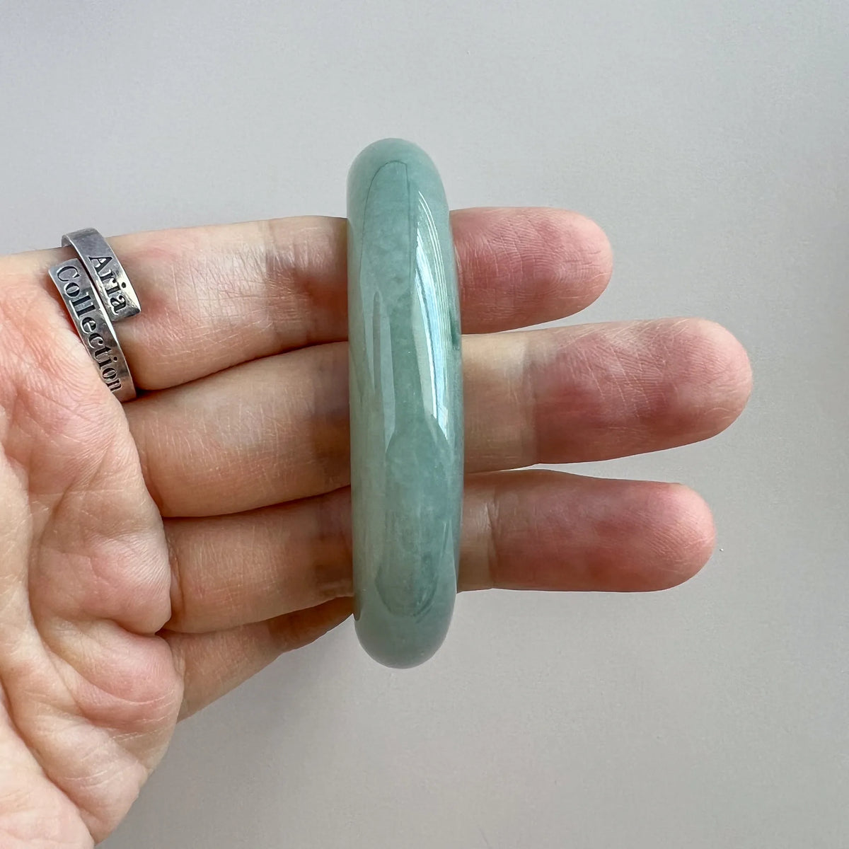 Side profile of the light green-blue jadeite bangle showing its rounded shape and glossy polished surface