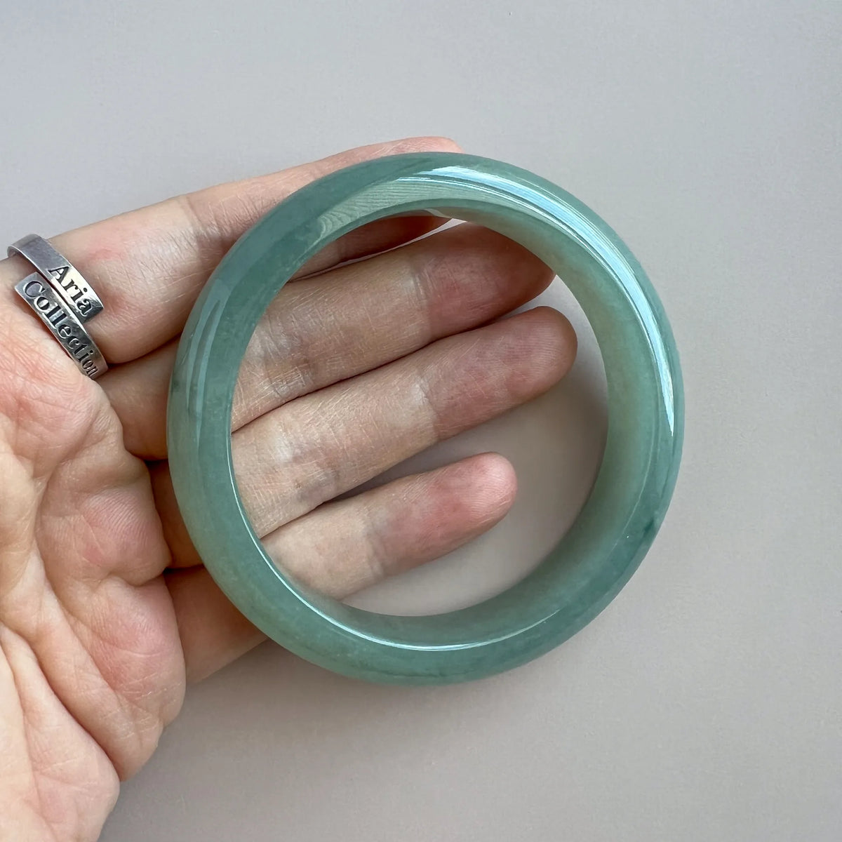 Hand-held front view of glossy green jade bangle showing translucent stone and even polish