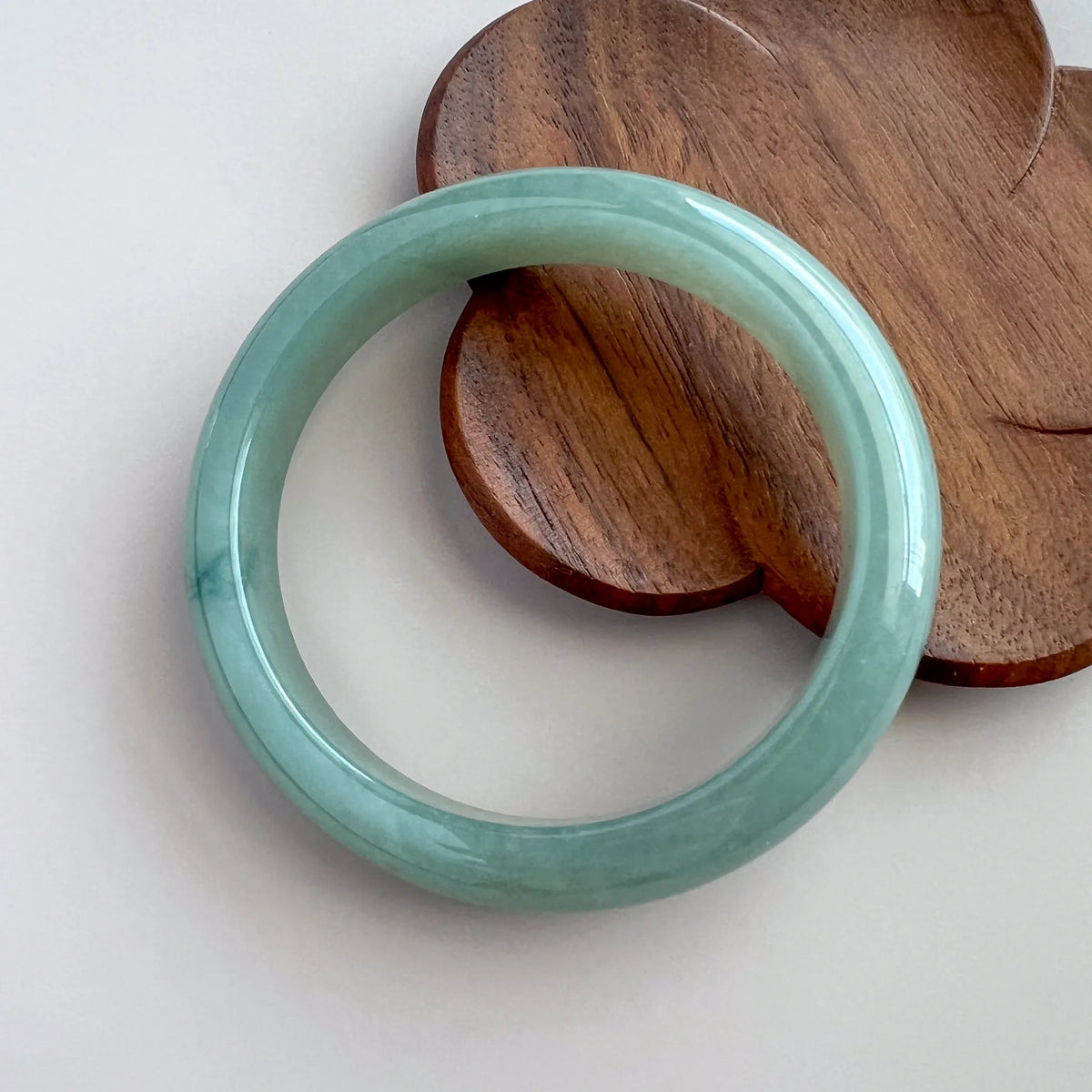 Polished green jade bangle styled with a wooden display board on a clean background