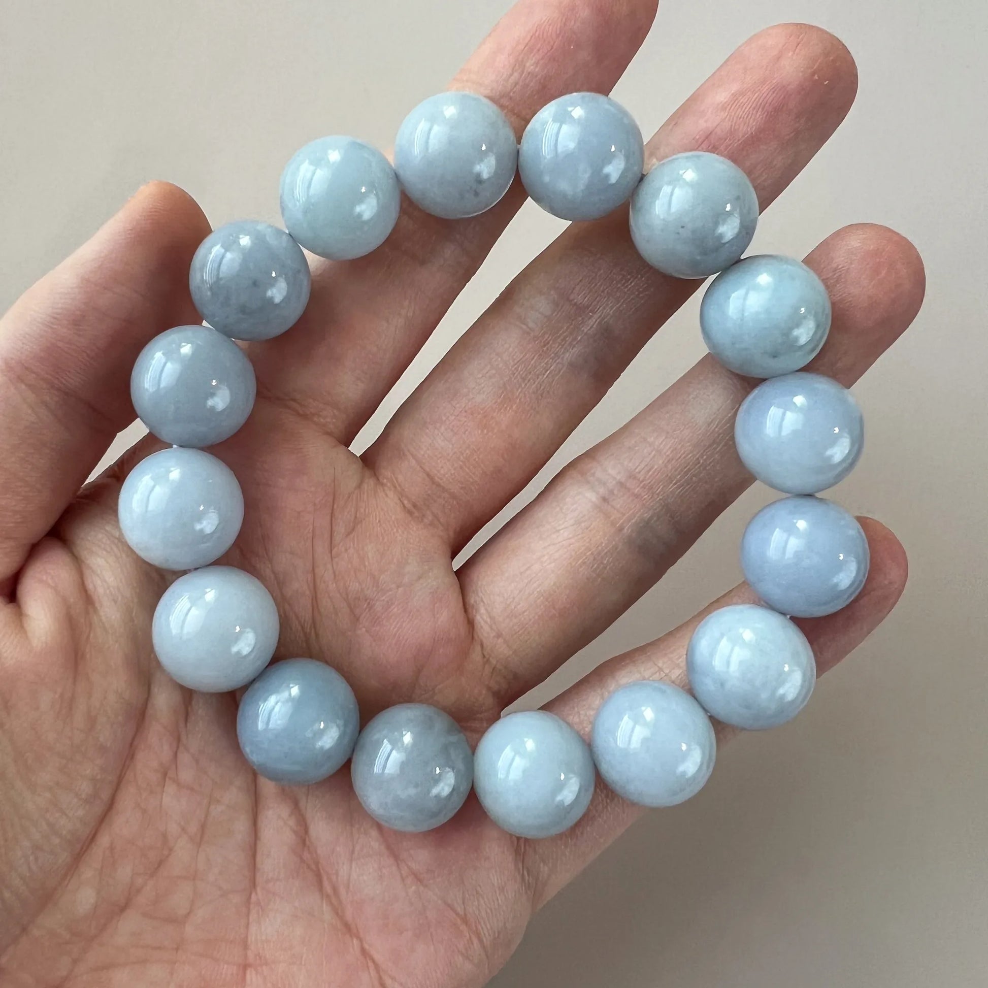 Blue beaded bracelet draped across fingers, glossy polished gemstone finish
