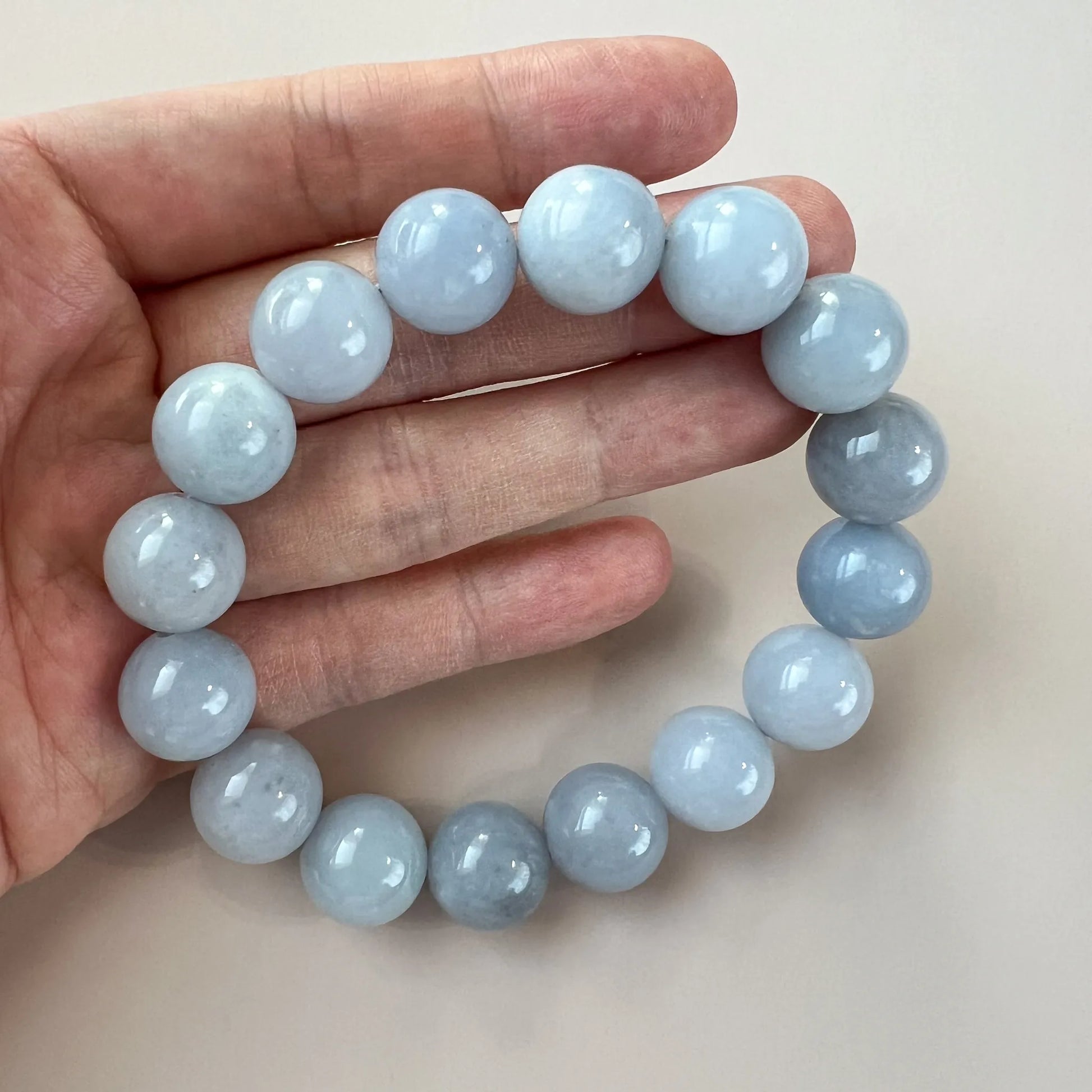 Round light blue bead bracelet held in hand, smooth polished stone beads