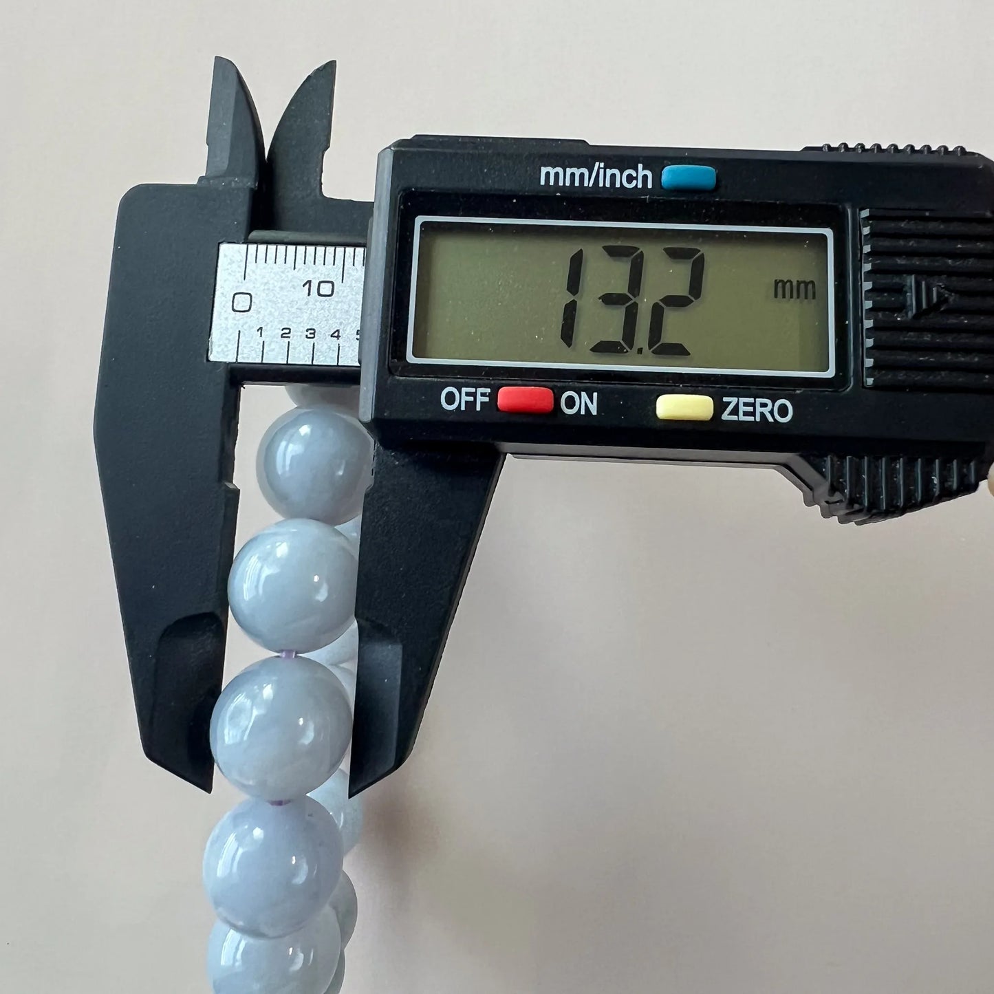 Digital caliper measuring a polished light blue jade bracelet bead at approximately 13.2mm