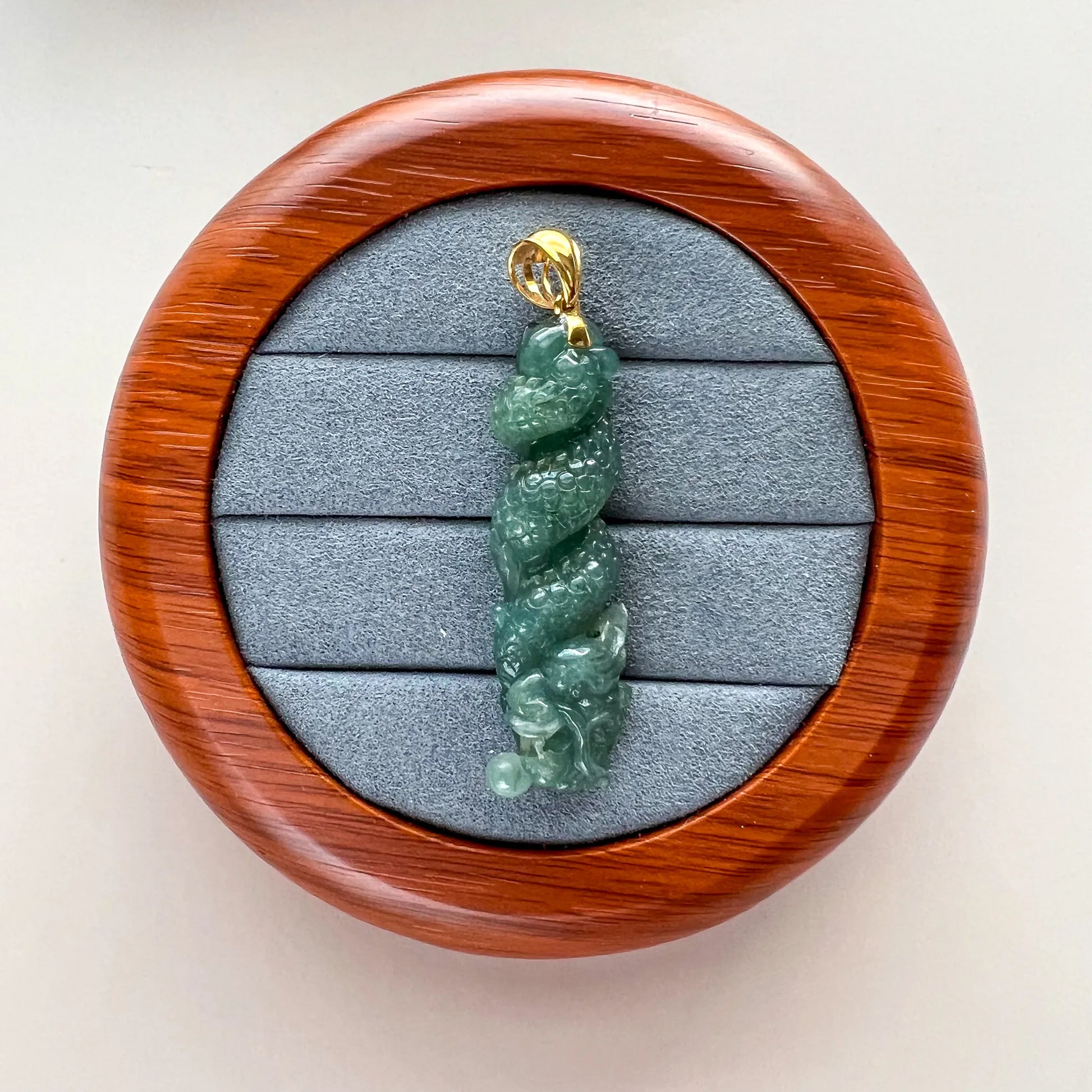 Front view of green carved jade pendant on gray velvet tray in round wood display