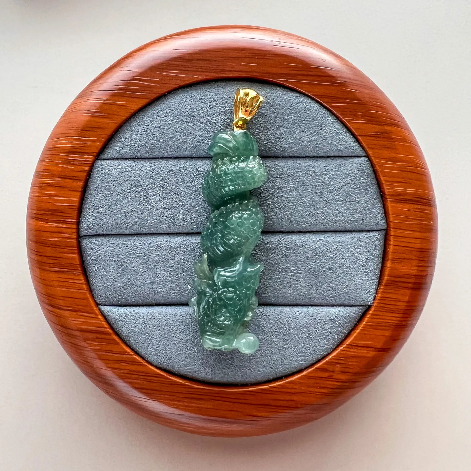 Side view of green carved jade pendant on gray velvet tray in round wood display