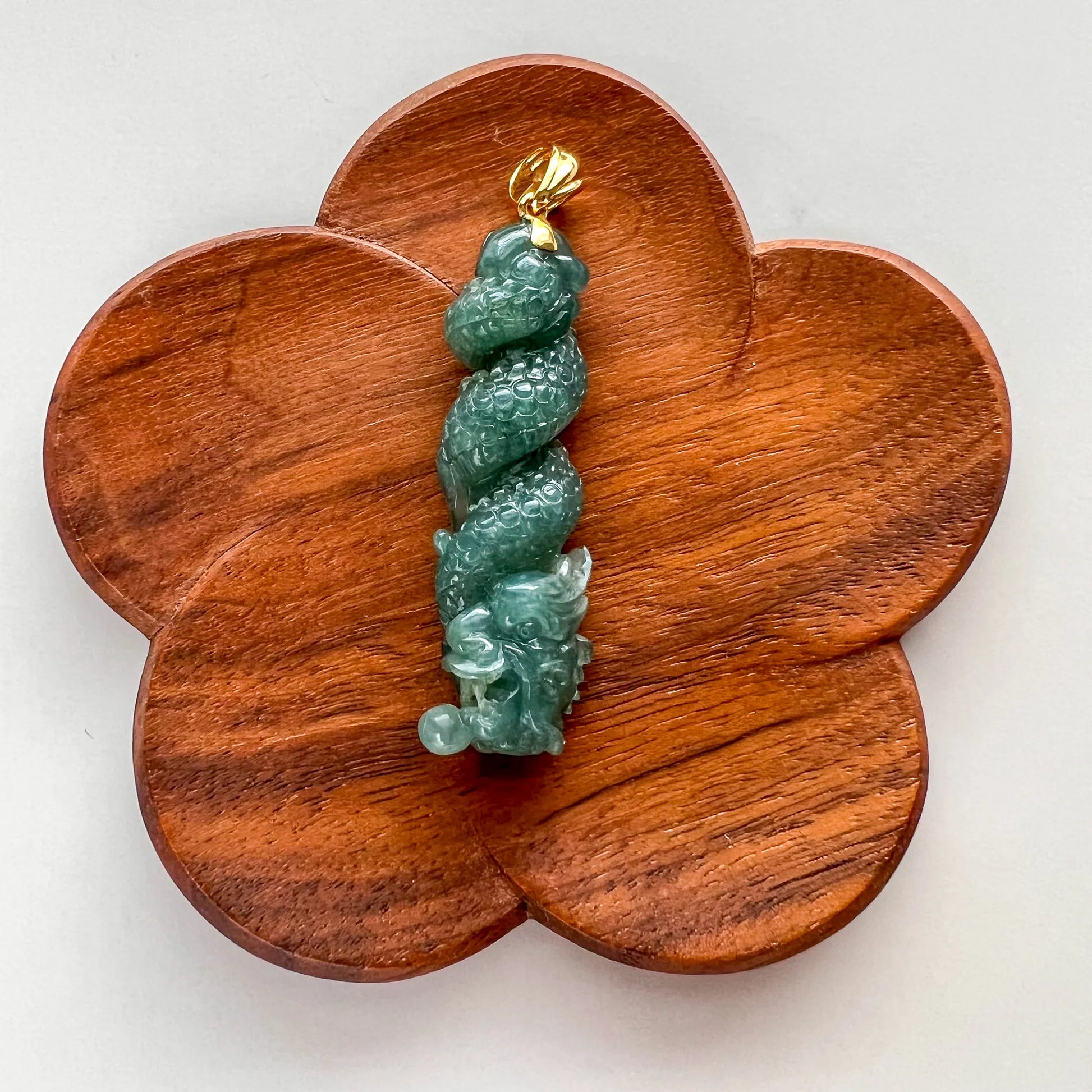 Front view of green carved jade pendant on flower-shaped wooden display base