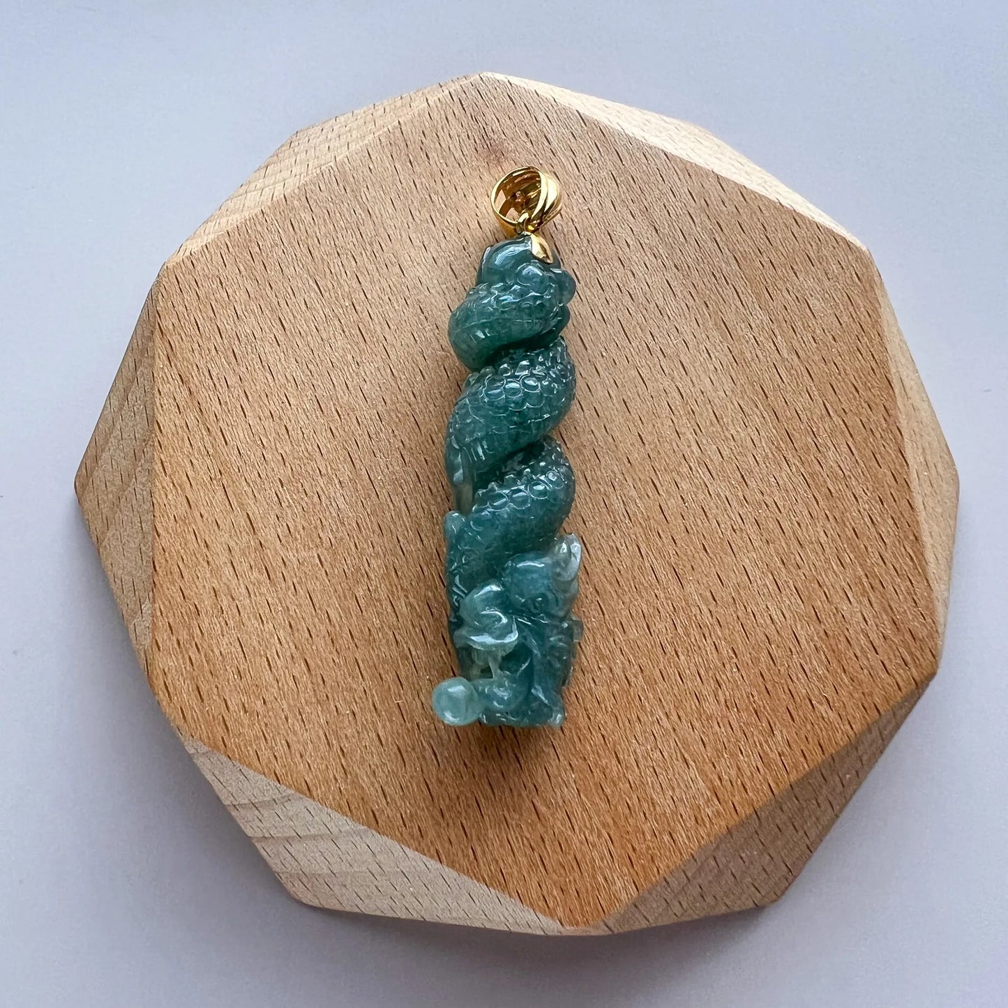 Front view of green carved jade pendant on faceted wooden display base