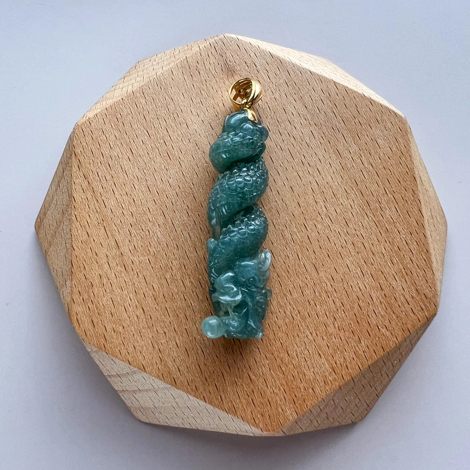 Front view of green carved jade pendant on faceted wooden display base