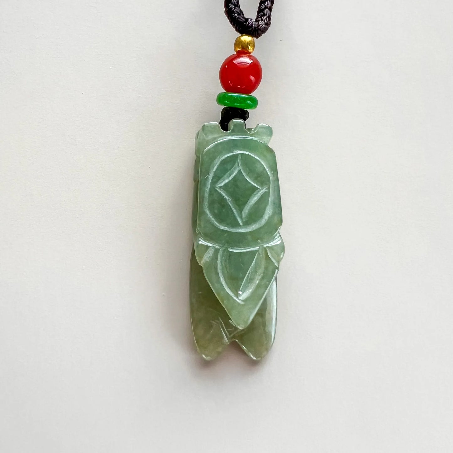 Back of light green natural jade cicada pendant with geometric carving and polished finish