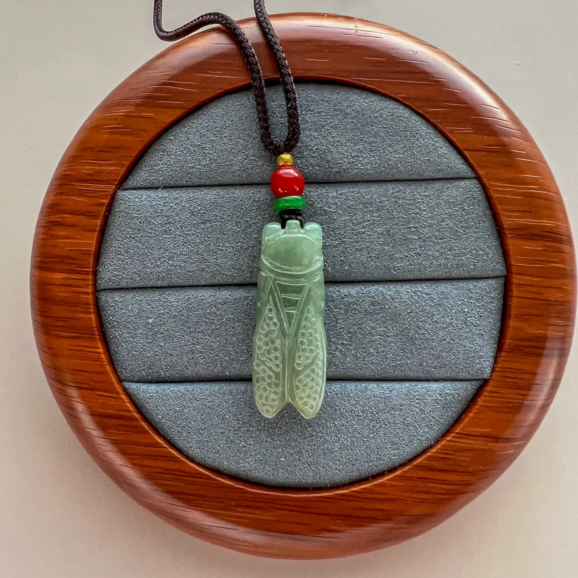 Pendant front on round wood display with carved green stone and multicolor cord beads