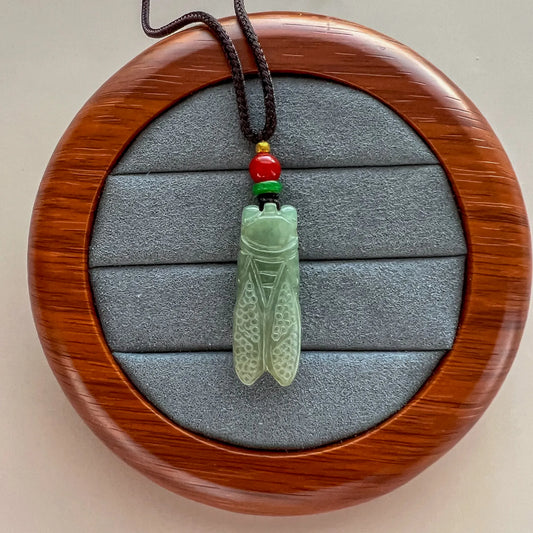 Pendant front on round wood display with carved green stone and multicolor cord beads