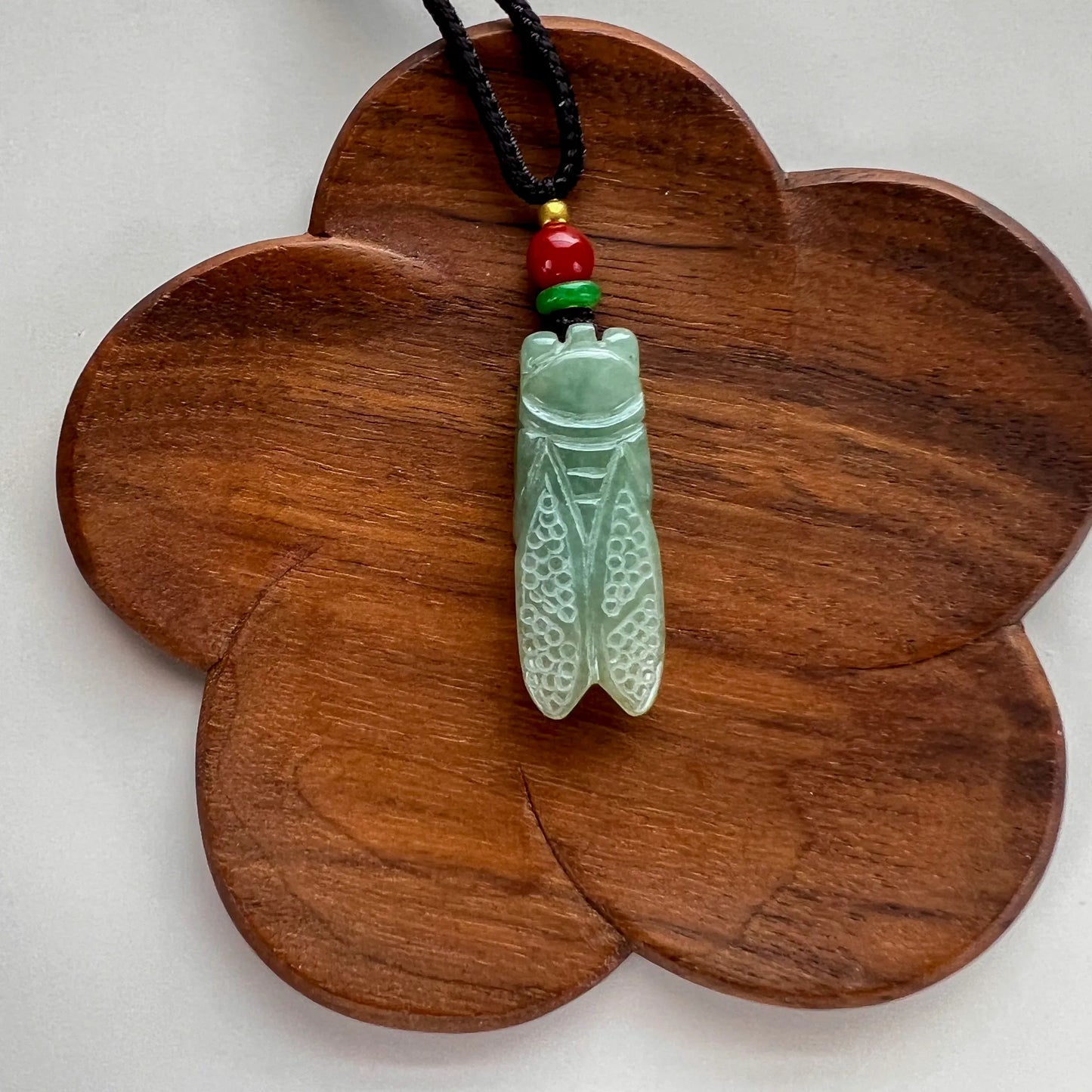 Pendant shown on flower-shaped wood display, polished green stone with carved insect detail