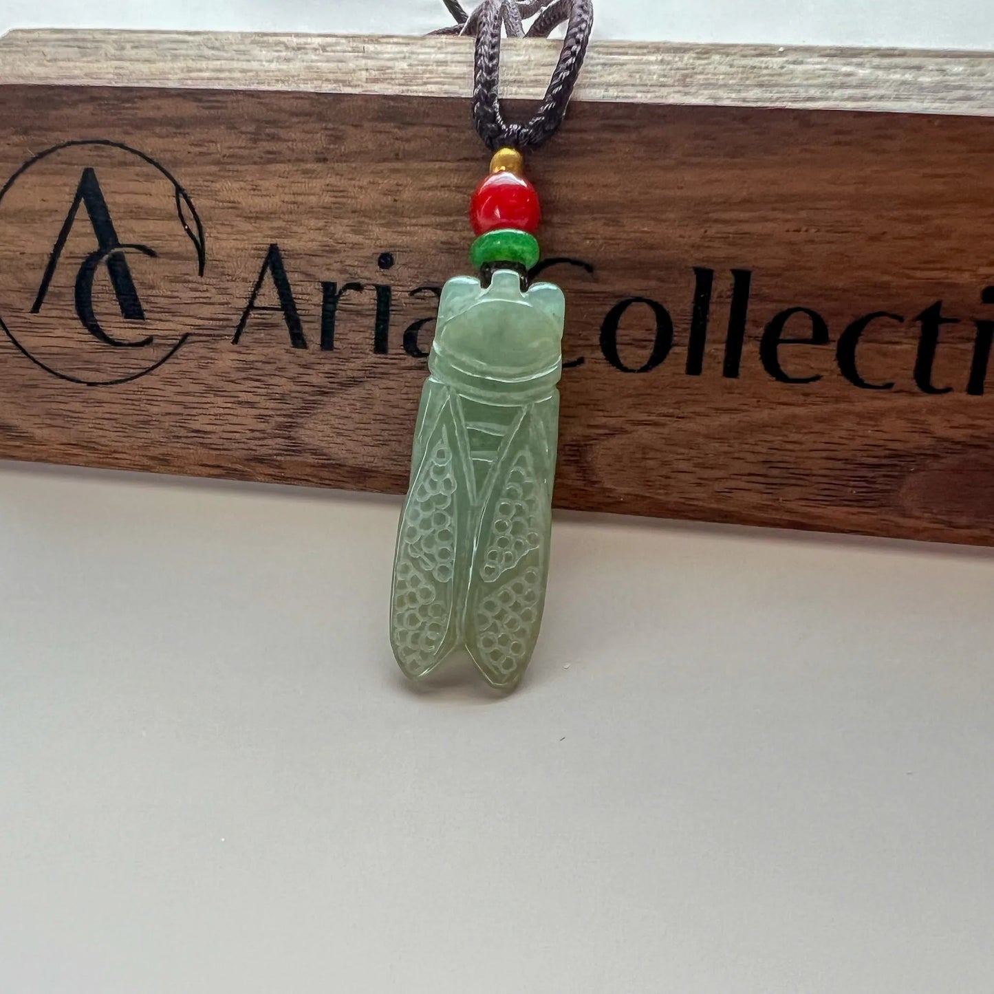 Green carved stone pendant hanging from cord on branded wood plaque, front view