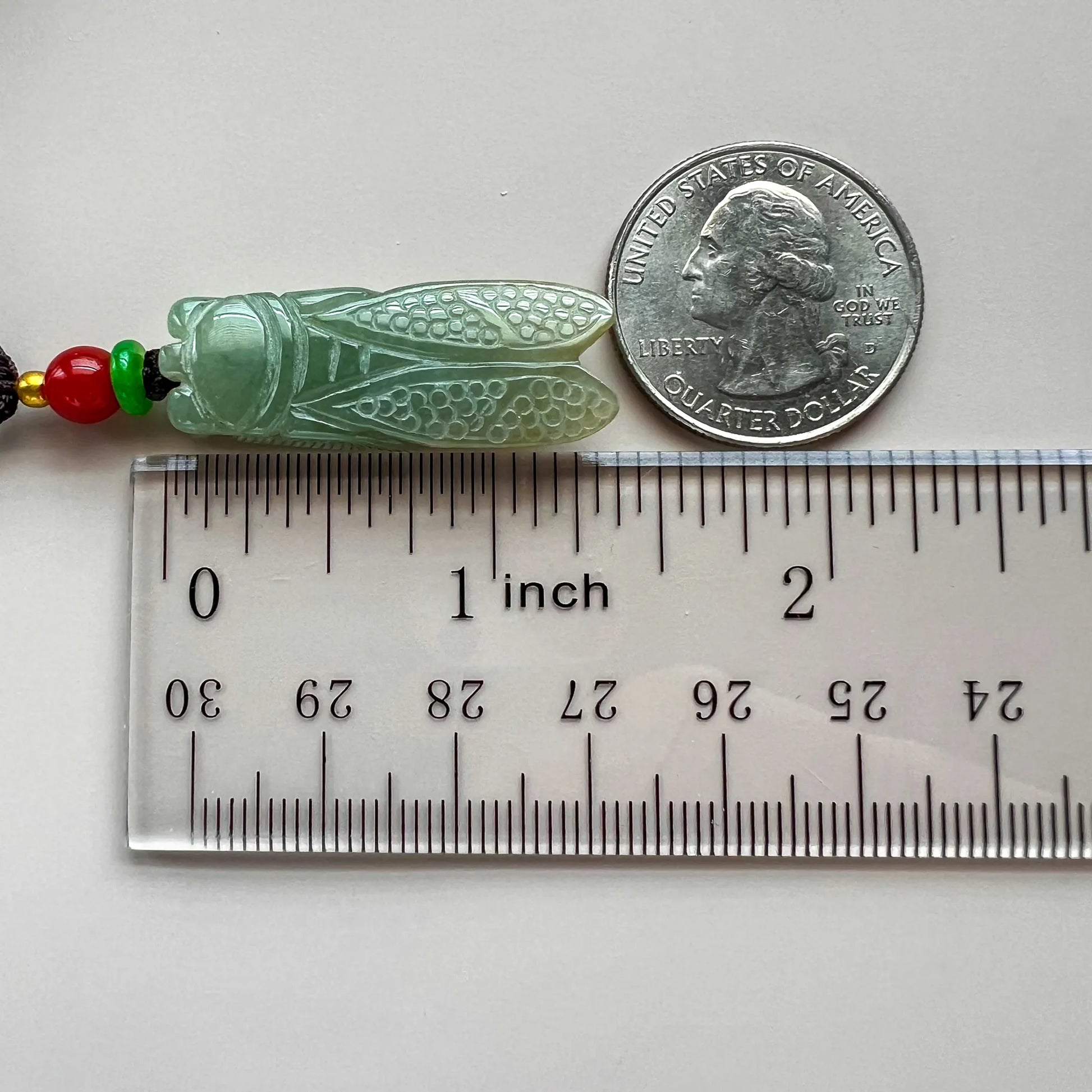 Side view of carved green stone pendant beside ruler and quarter for scale
