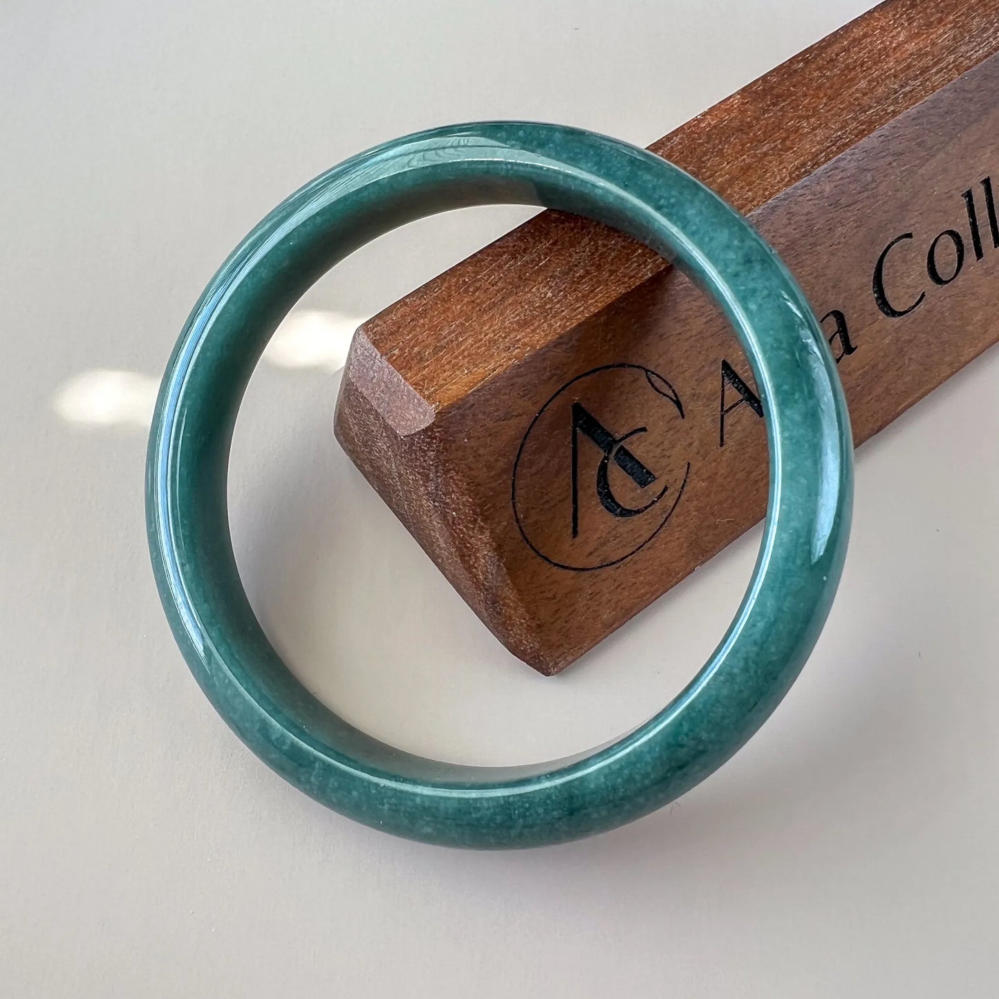 Glossy green jade bangle on wooden display block, front view