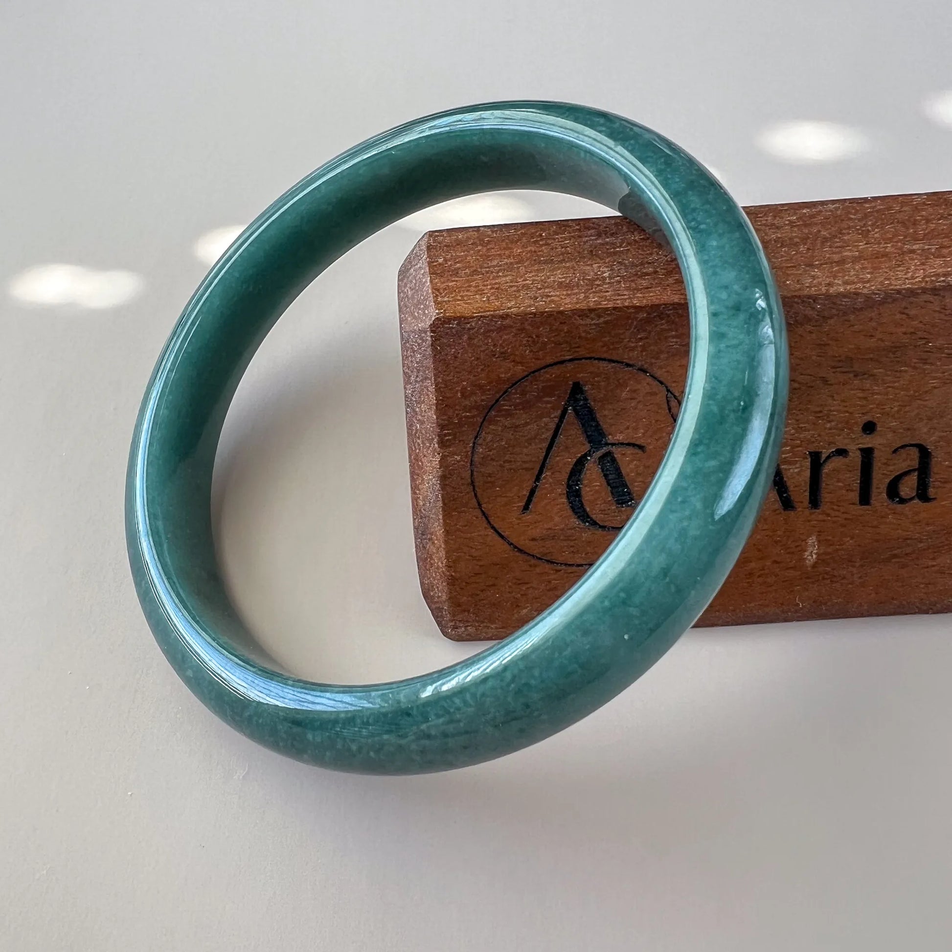 Polished green jade bangle angled on a wooden stand, smooth round profile
