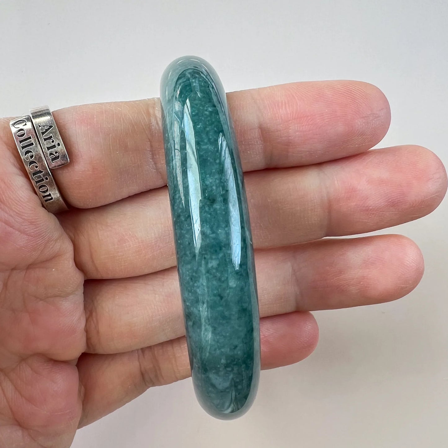 Side view of a slim green jade bangle held in hand, high-gloss finish