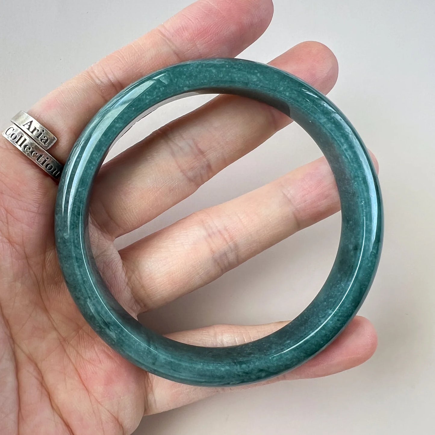 Front view of a green jade bangle held in hand, polished round shape