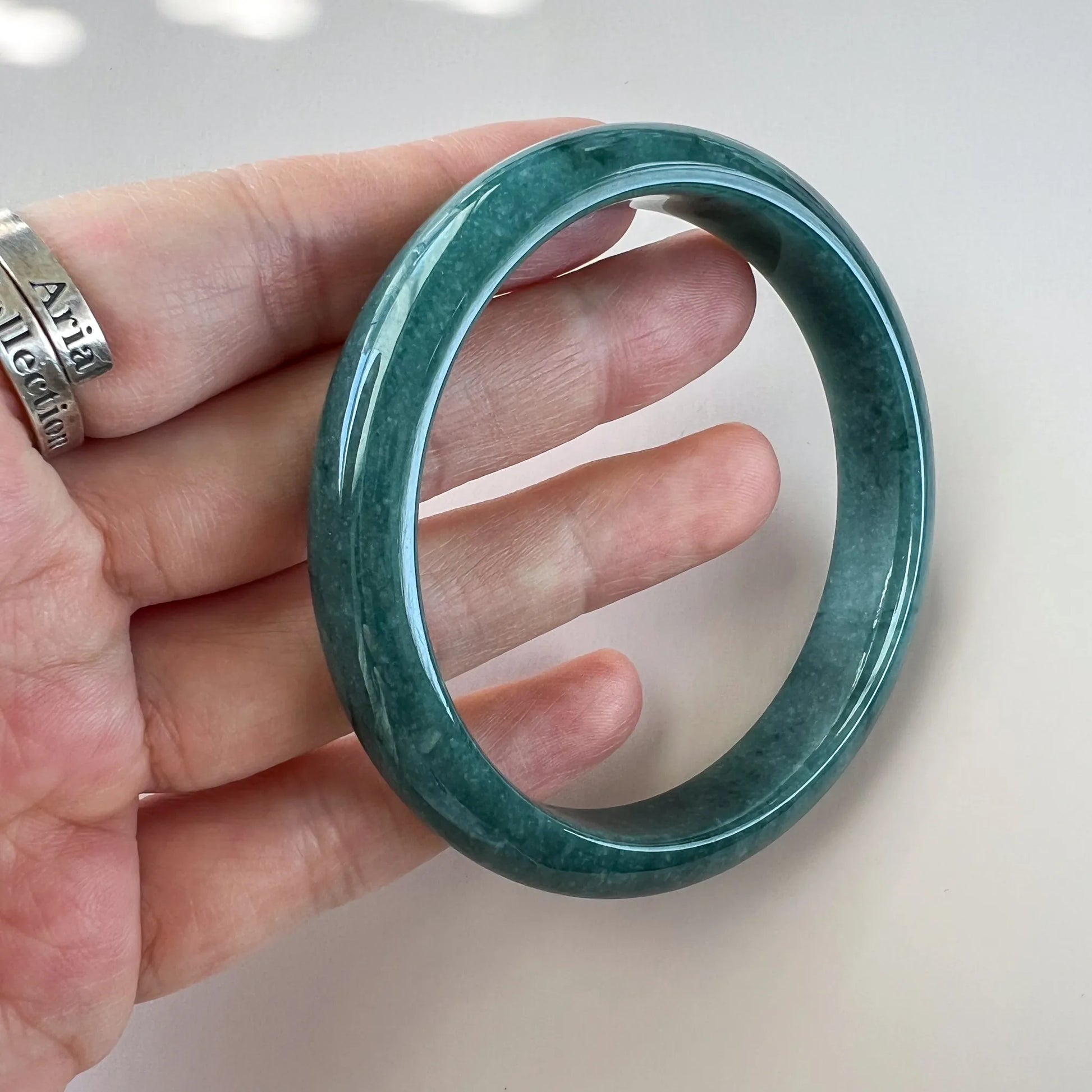 Open front view of a green jade bangle held in hand, translucent polish