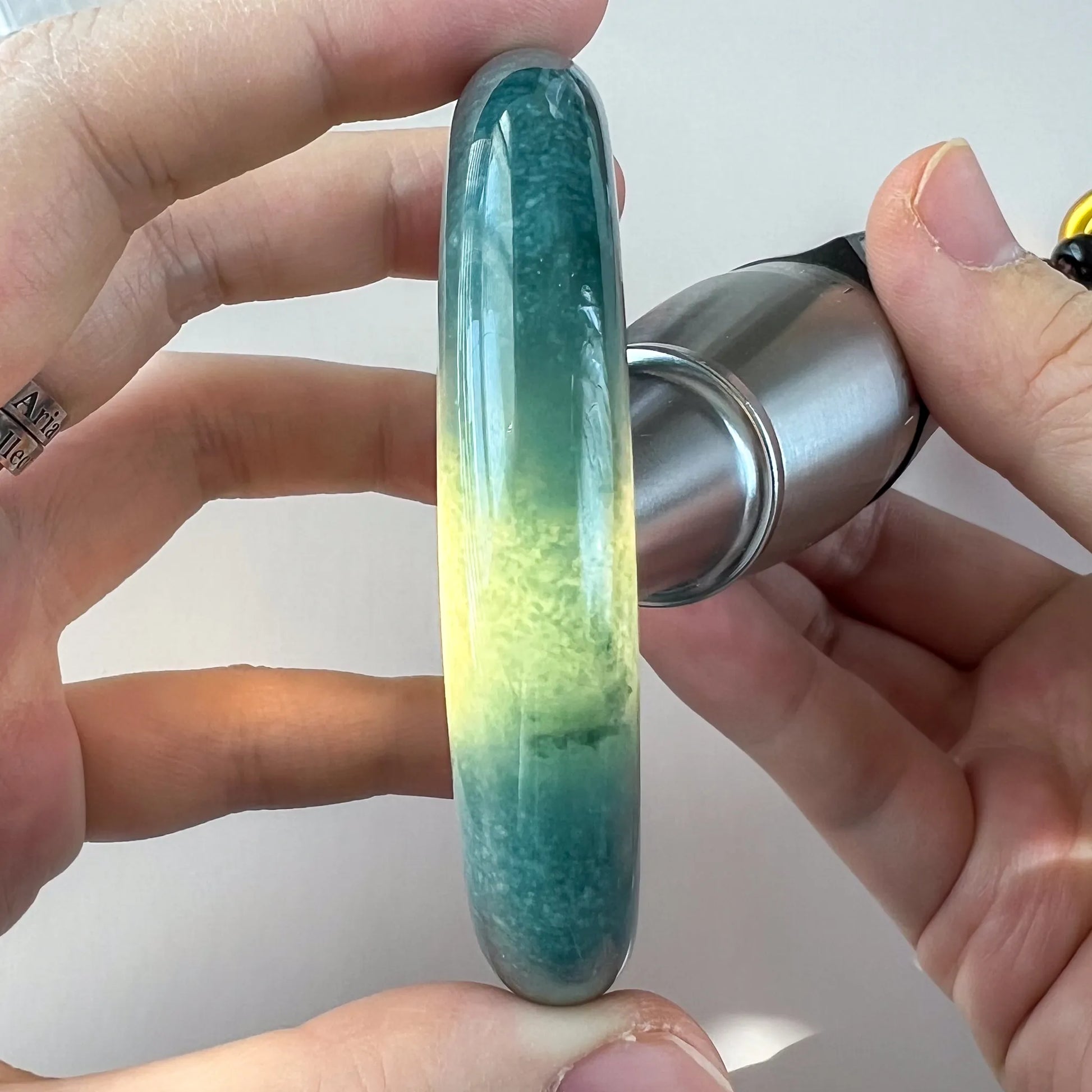 Side view of a green-to-yellow jade bangle under light, glossy carved surface