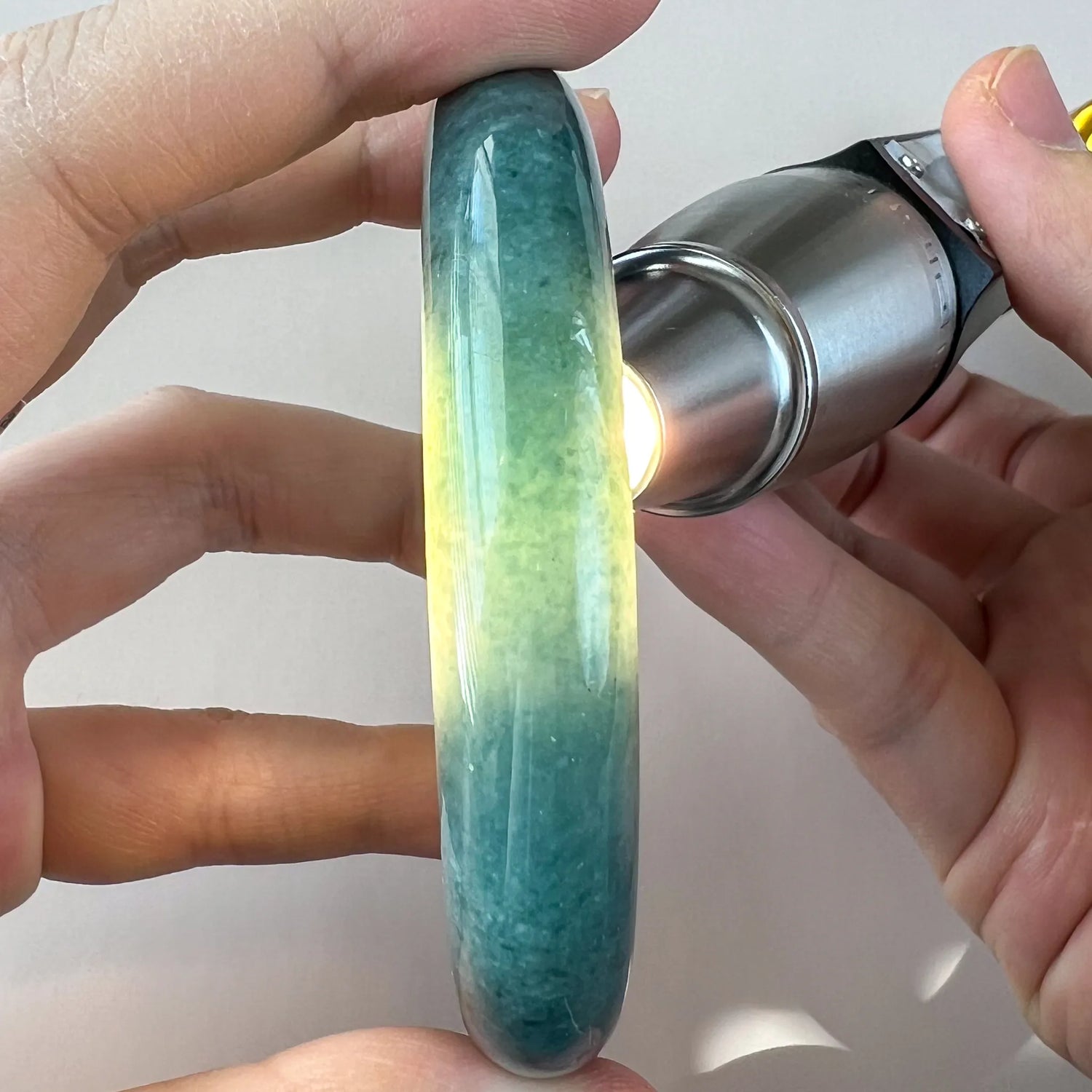 Backlit side view of a translucent green jade bangle showing color variation